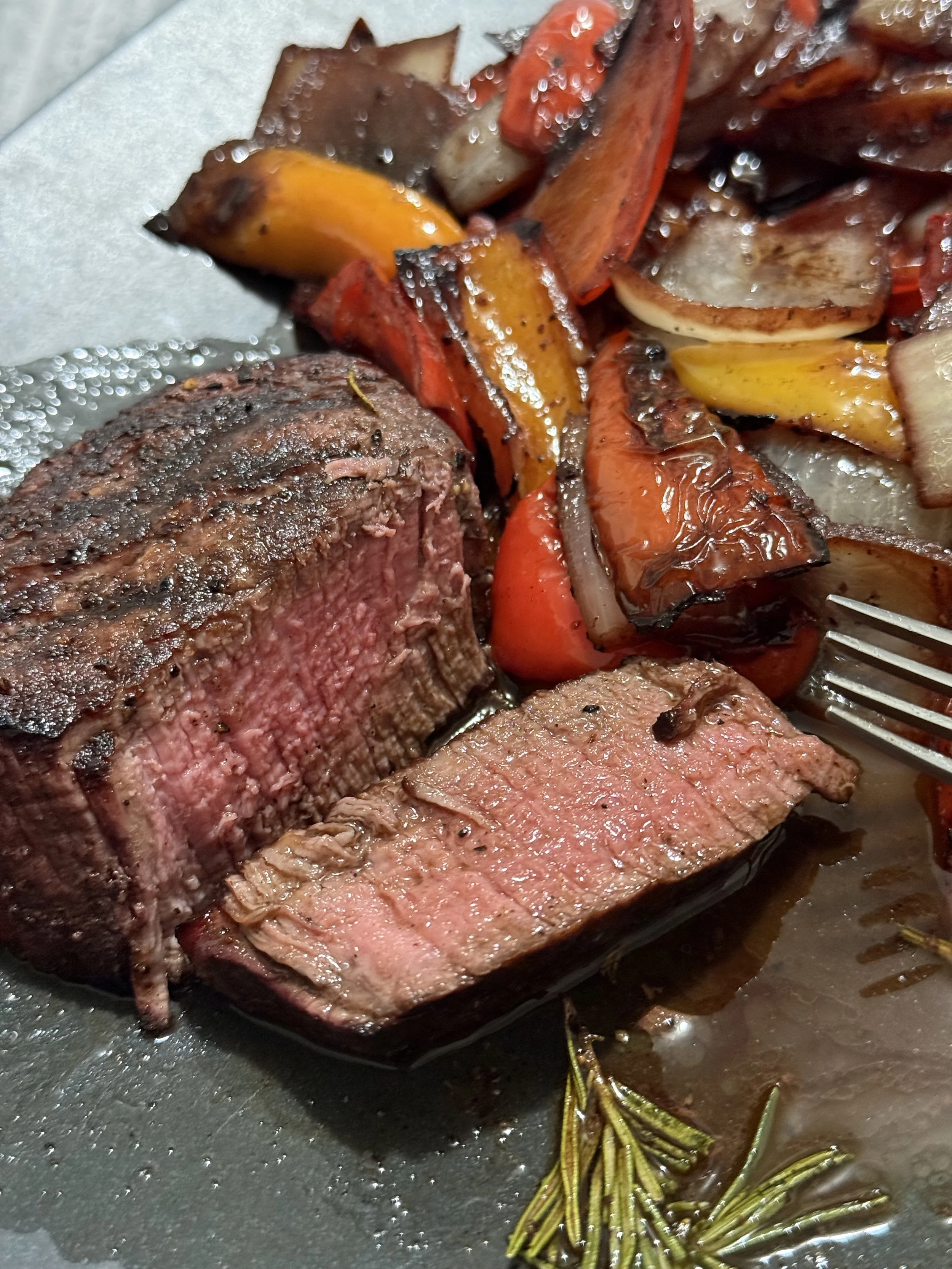 Cooked beef steak with grilled vegetables including peppers, onions, and zucchini, garnished with rosemary.