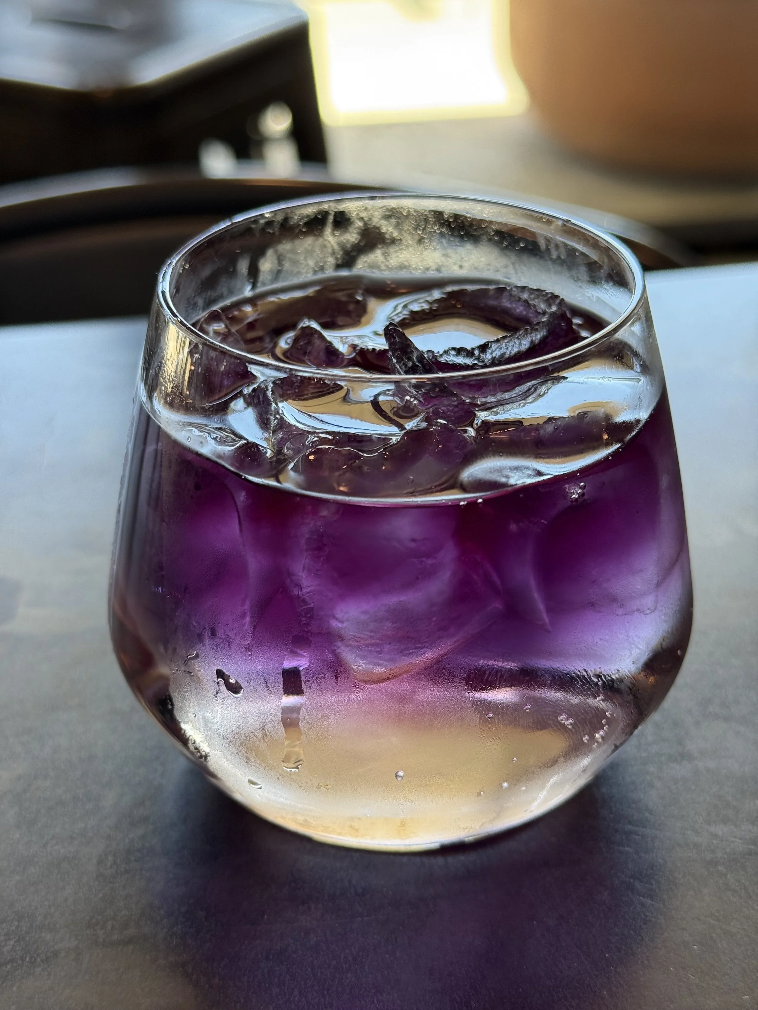 Glass of purple-colored beverage with ice cubes, sitting on a table.