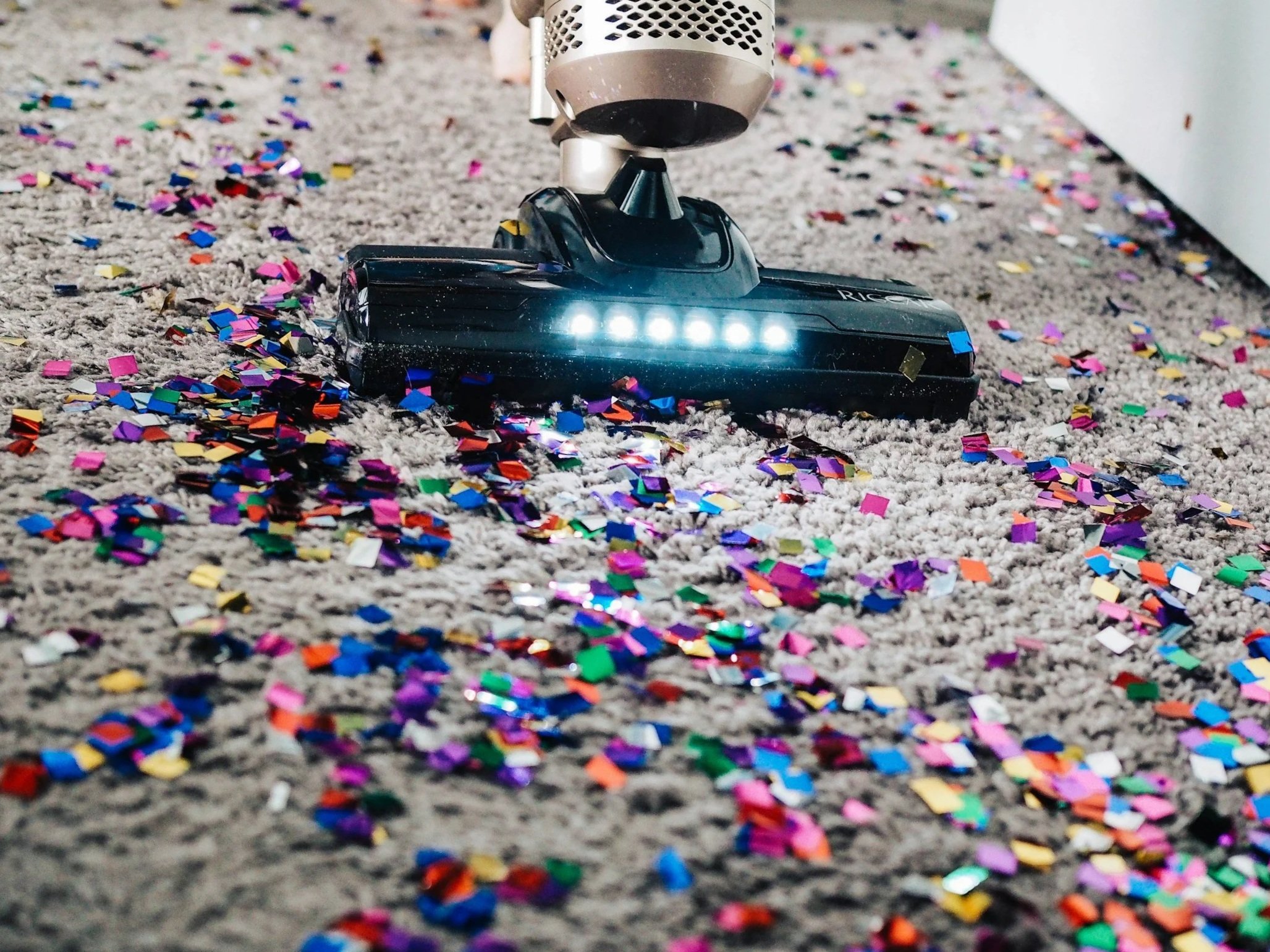A vacuum cleaner on a carpet, sweeping up colorful confetti.