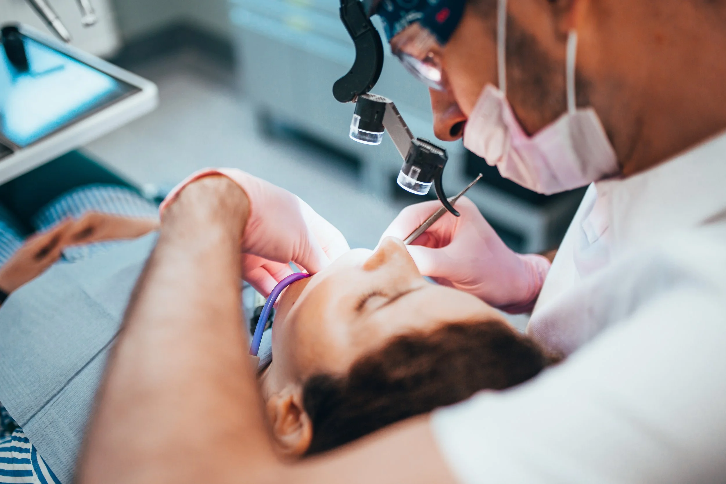 A dentist examining a patient's mouth with a headlamp, using dental tools in a clinic.
