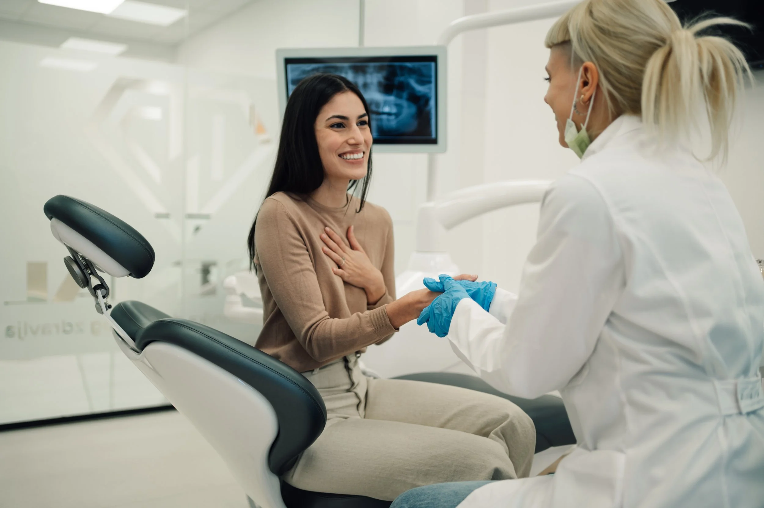 A woman sitting in a dental chair smiling while a female dentist shakes her hand in a dental clinic.