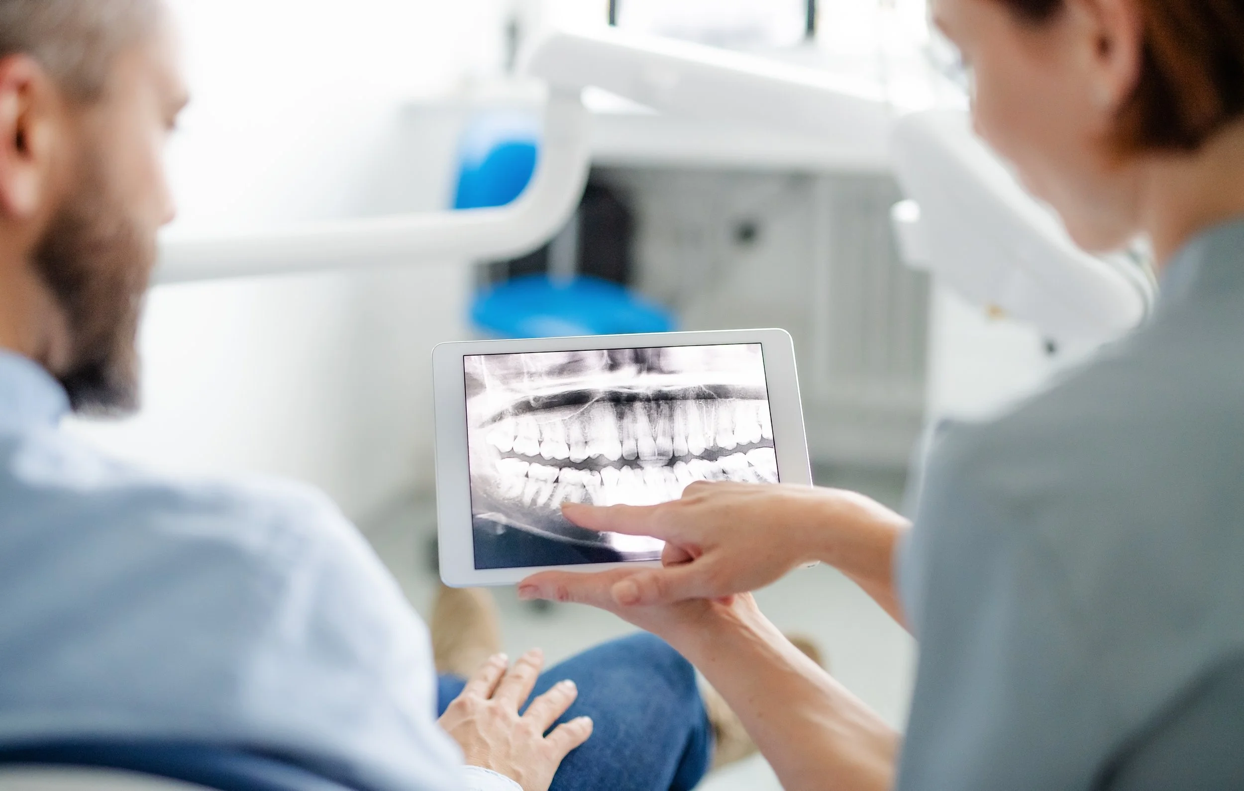 Dentist showing a patient an x-ray of their teeth on a tablet in a dental office.