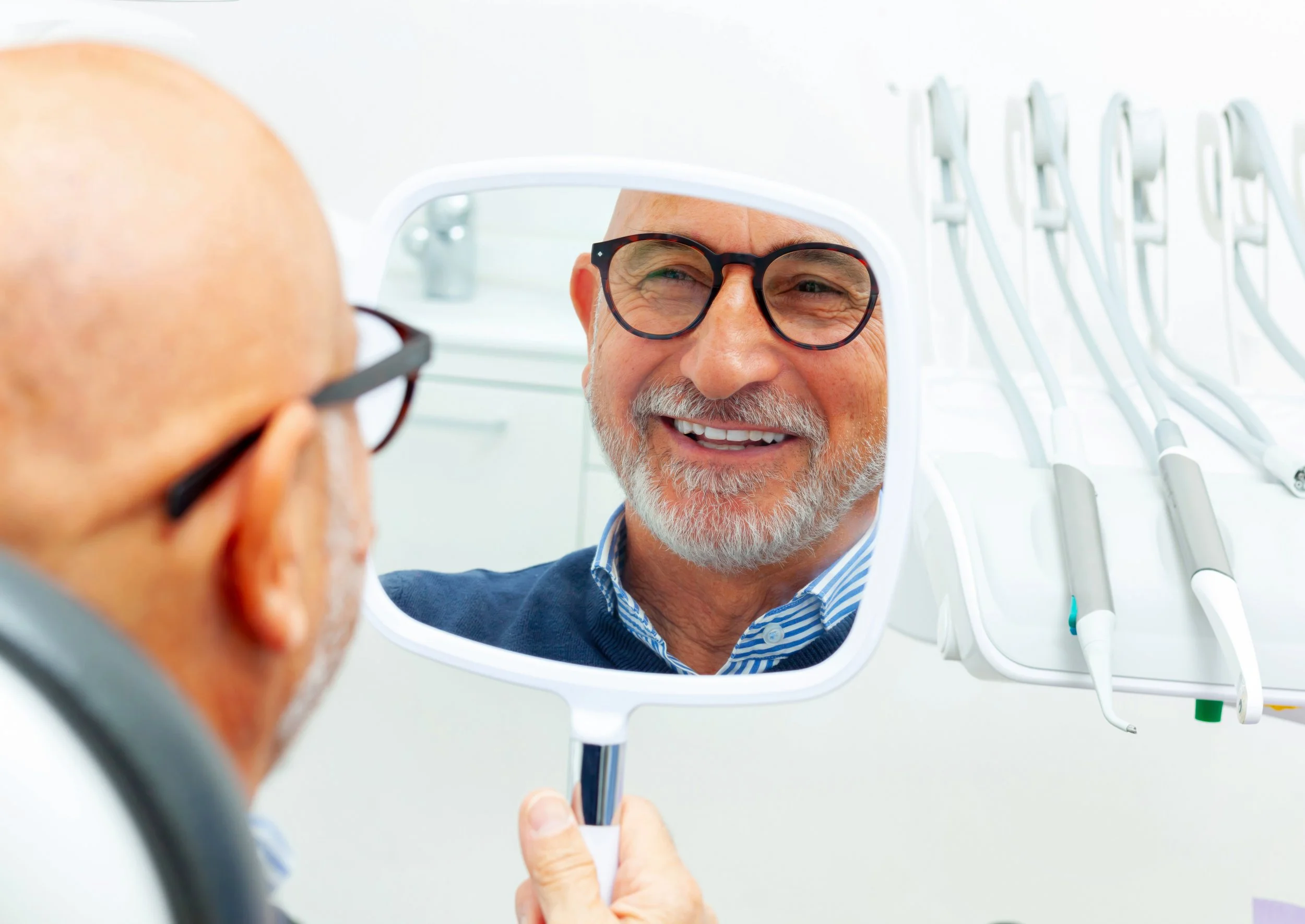 A smiling man looking at himself in a mirror at the dentist's office.