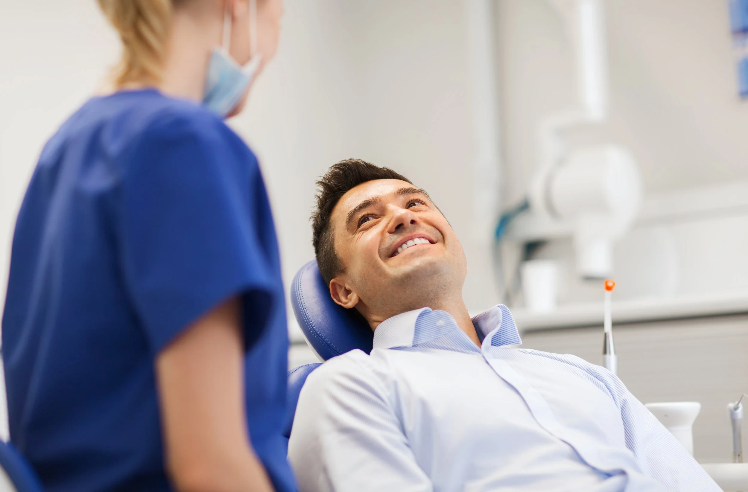 A man sitting in a dental chair smiling at a dental hygienist in a dental office.