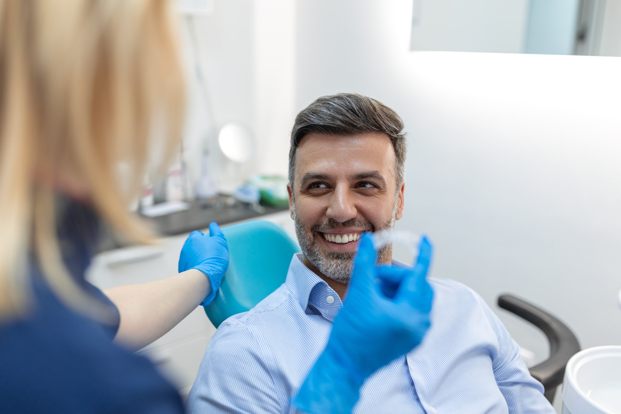 Smiling middle-aged man in a dress shirt receiving a vaccination from a healthcare professional wearing blue gloves in a medical office.