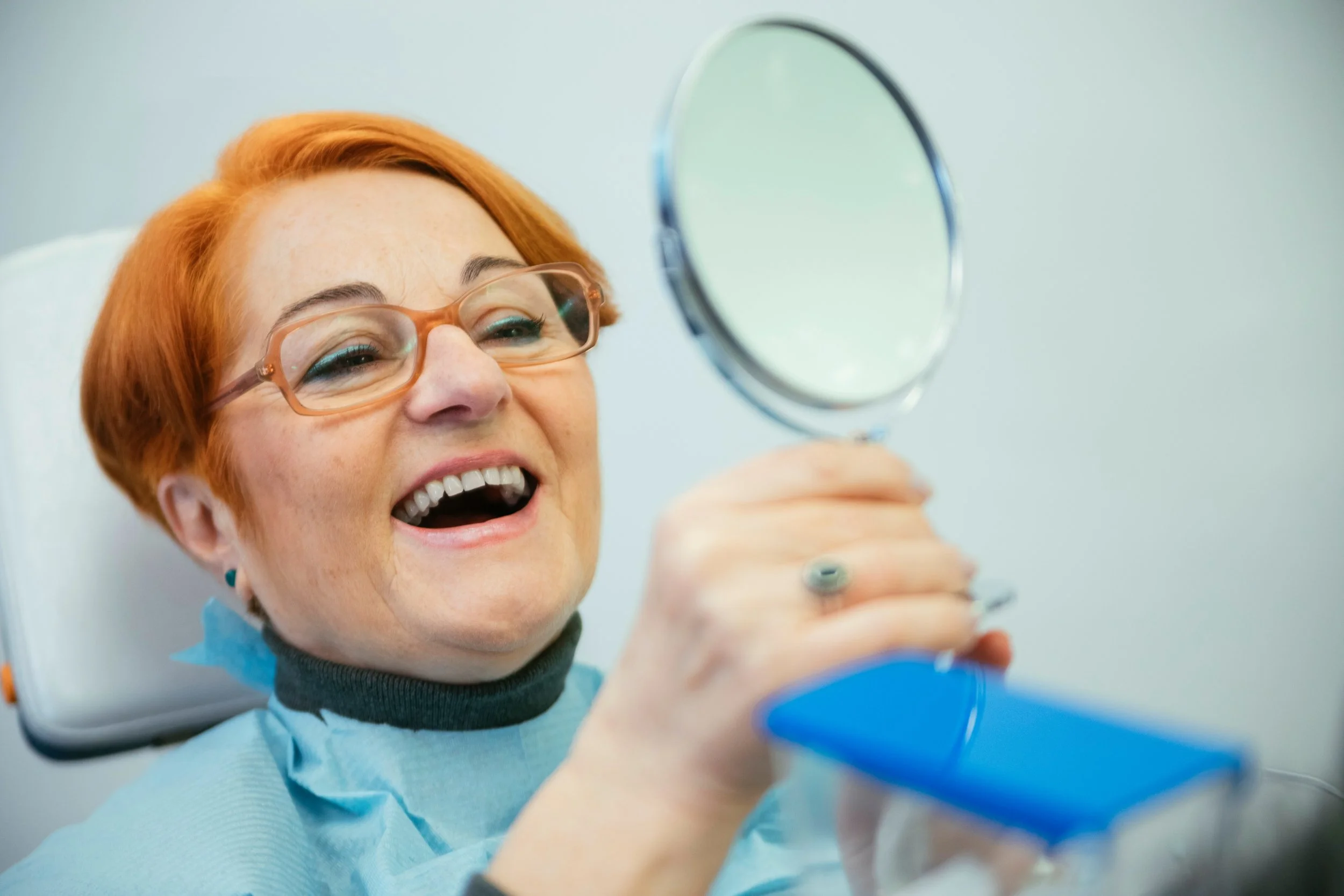 Woman smiling while holding a mirror in a dental office.