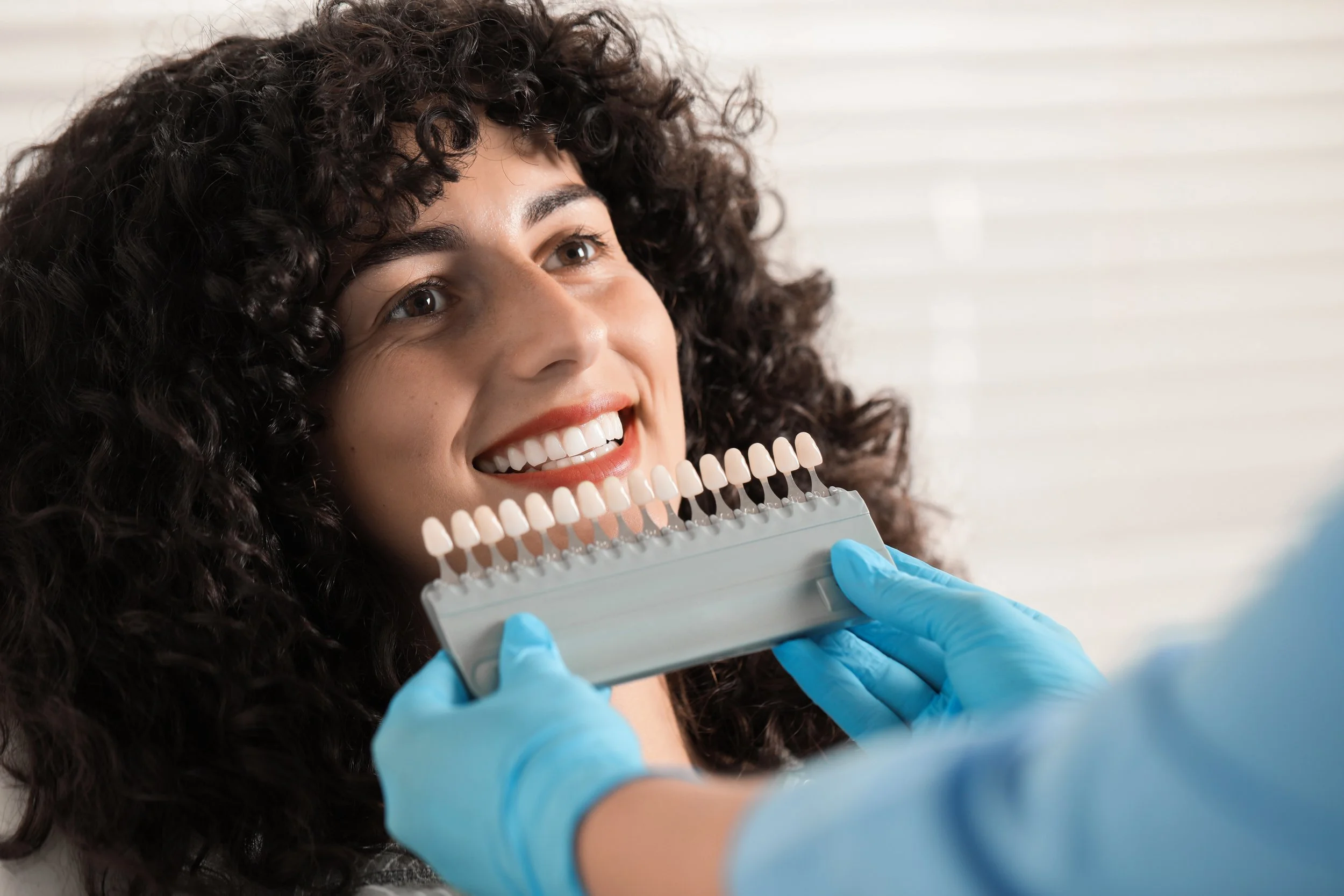 A woman smiling at a dental professional holding a shade guide for matching teeth colour.