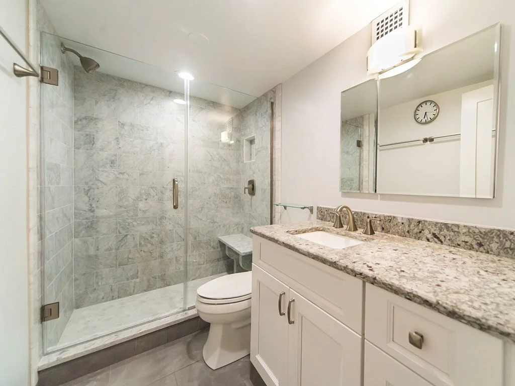 Bathroom with a glass-enclosed shower, toilet, white vanity with granite countertop, and a mirror above the sink.