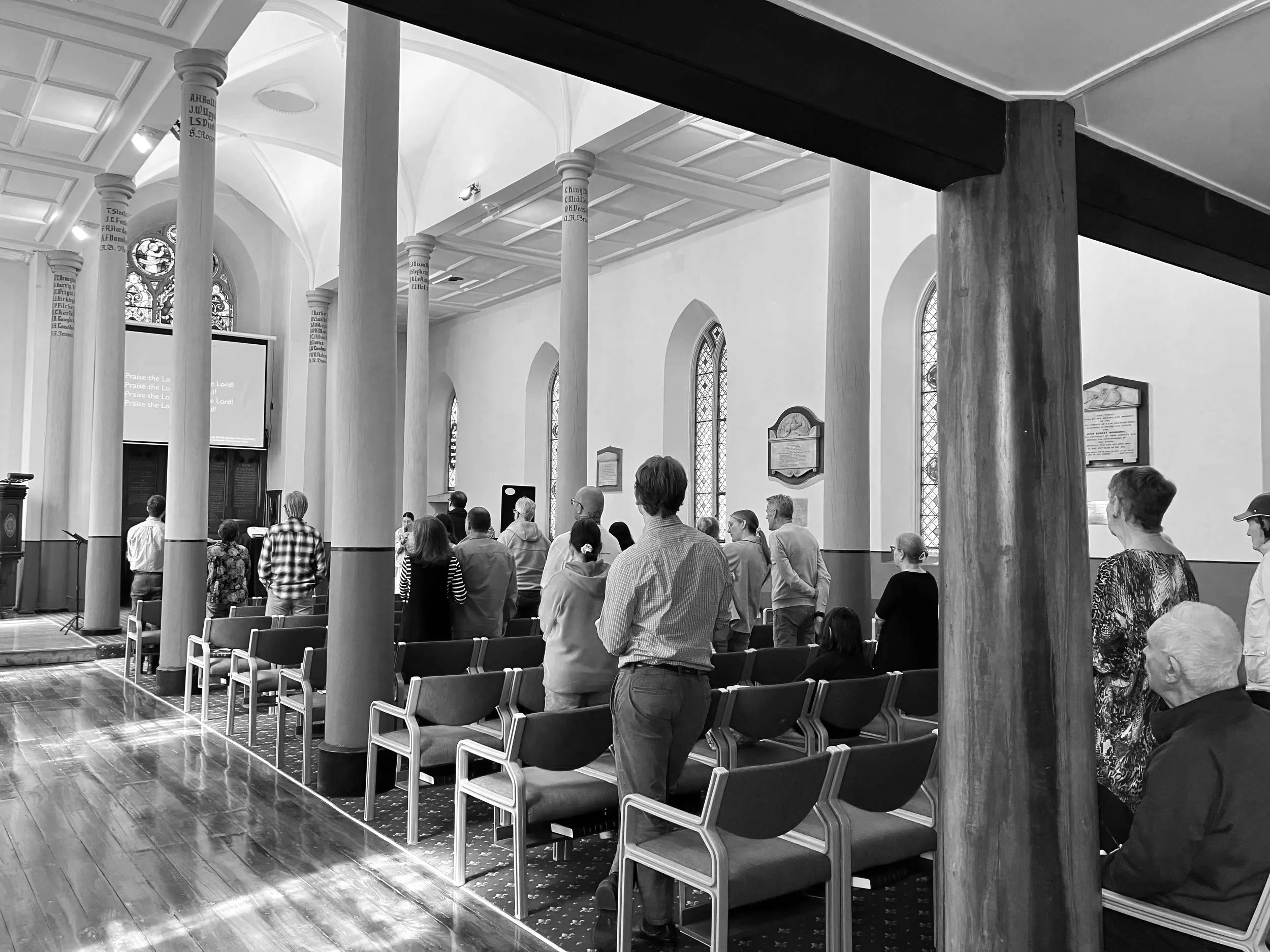 Interior of a church with tall columns, arched windows, and people gathered for a service or event.