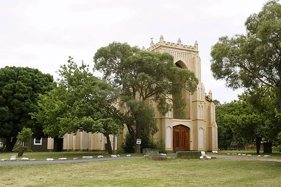 Historic church with a large wooden door, surrounded by trees in a grassy area.