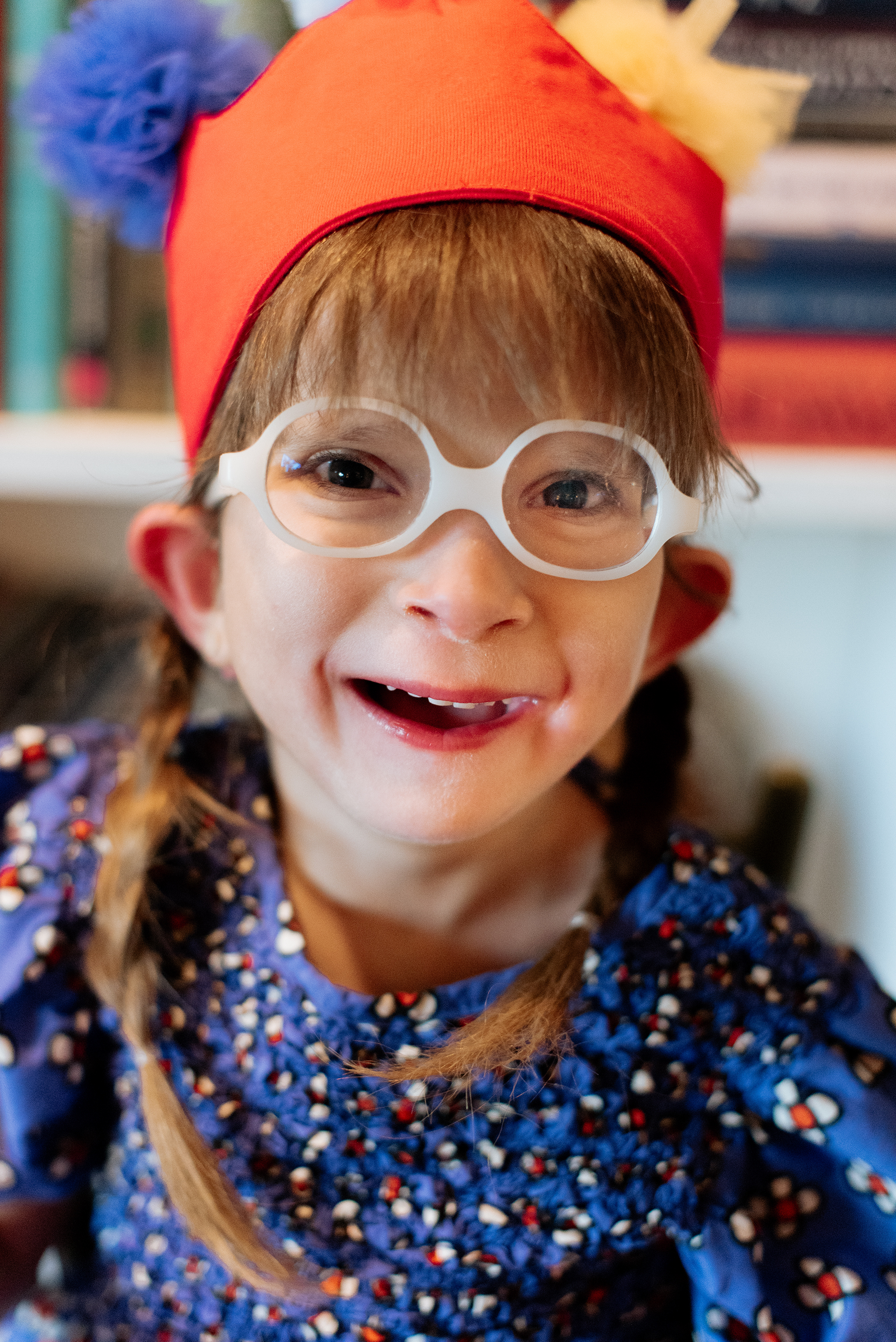 A young girl with glasses, wearing a red hat with plush animal ears, smiling at the camera.