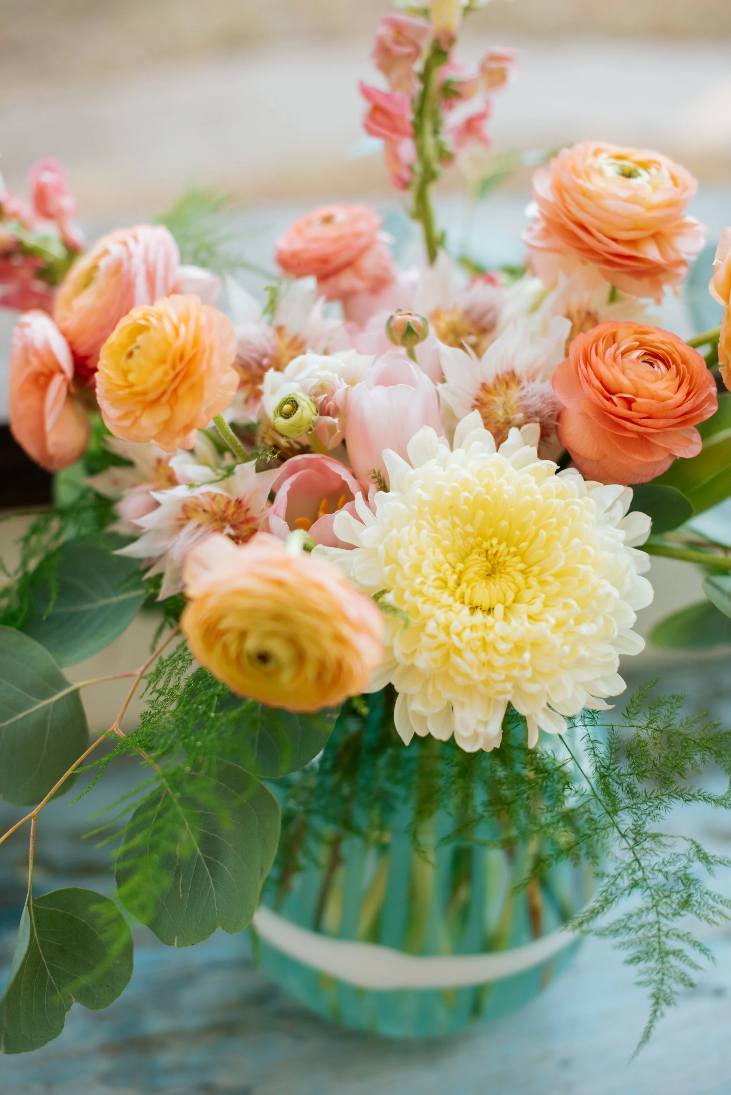 A bouquet of peach and white flowers in a turquoise and white striped vase.