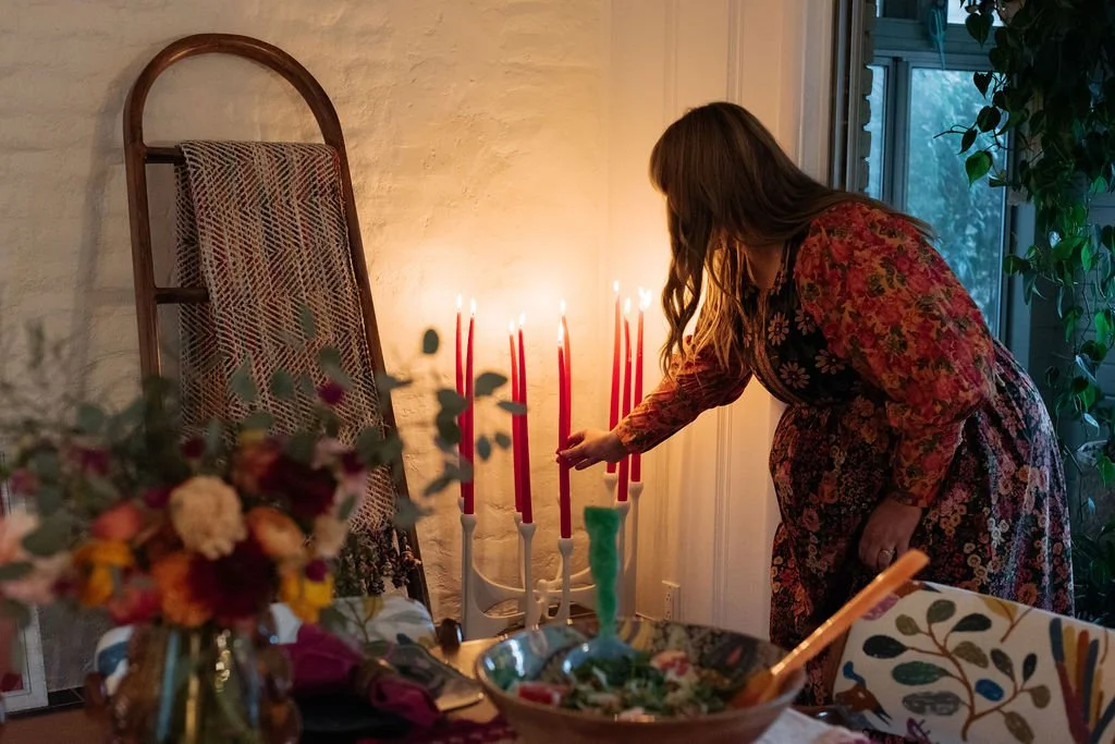 Woman lighting a red candle on a menorah during Hanukkah celebration inside a home.