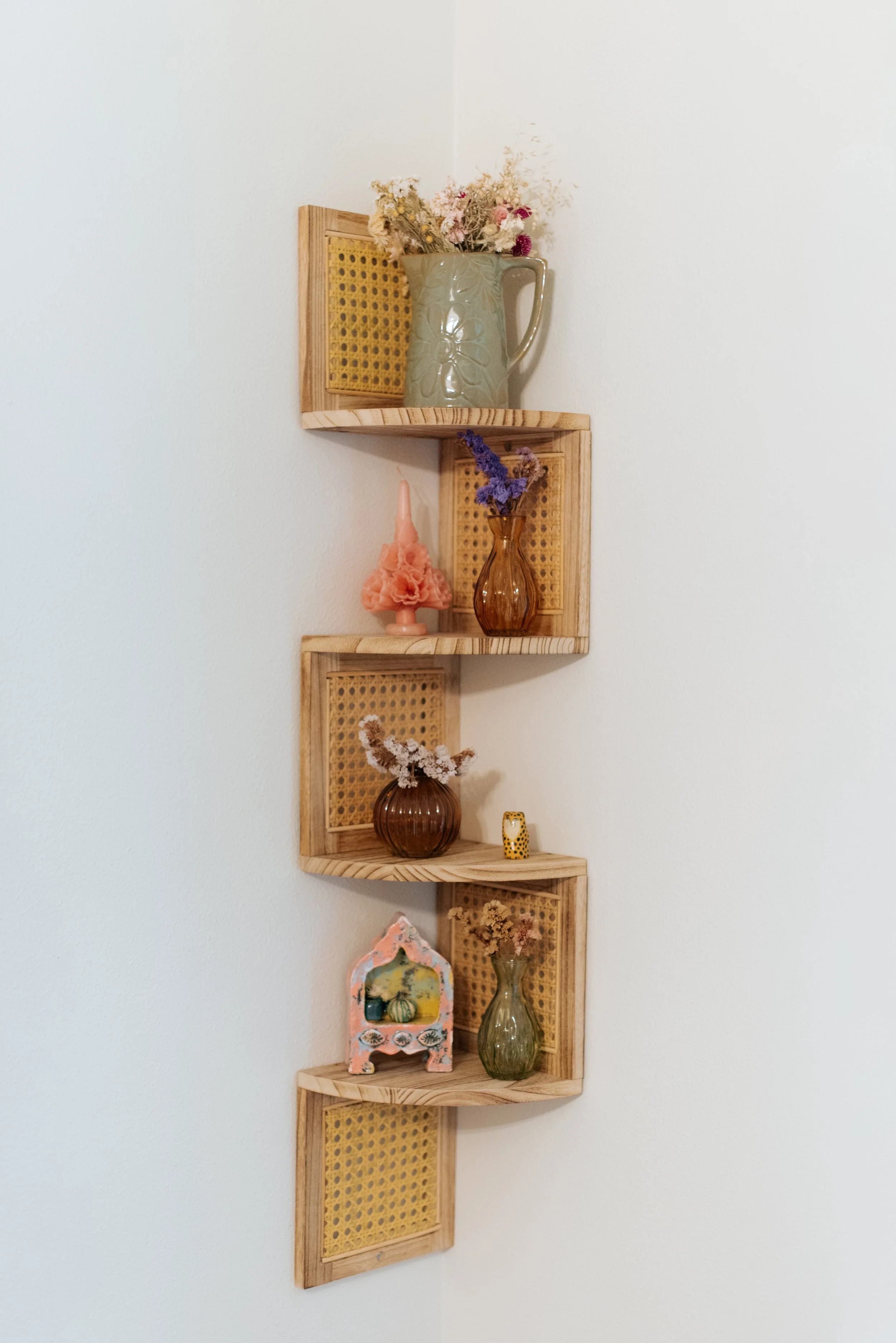 Decorative wooden wall shelf with five sections, holding various vases with dried flowers and a small decorative house.