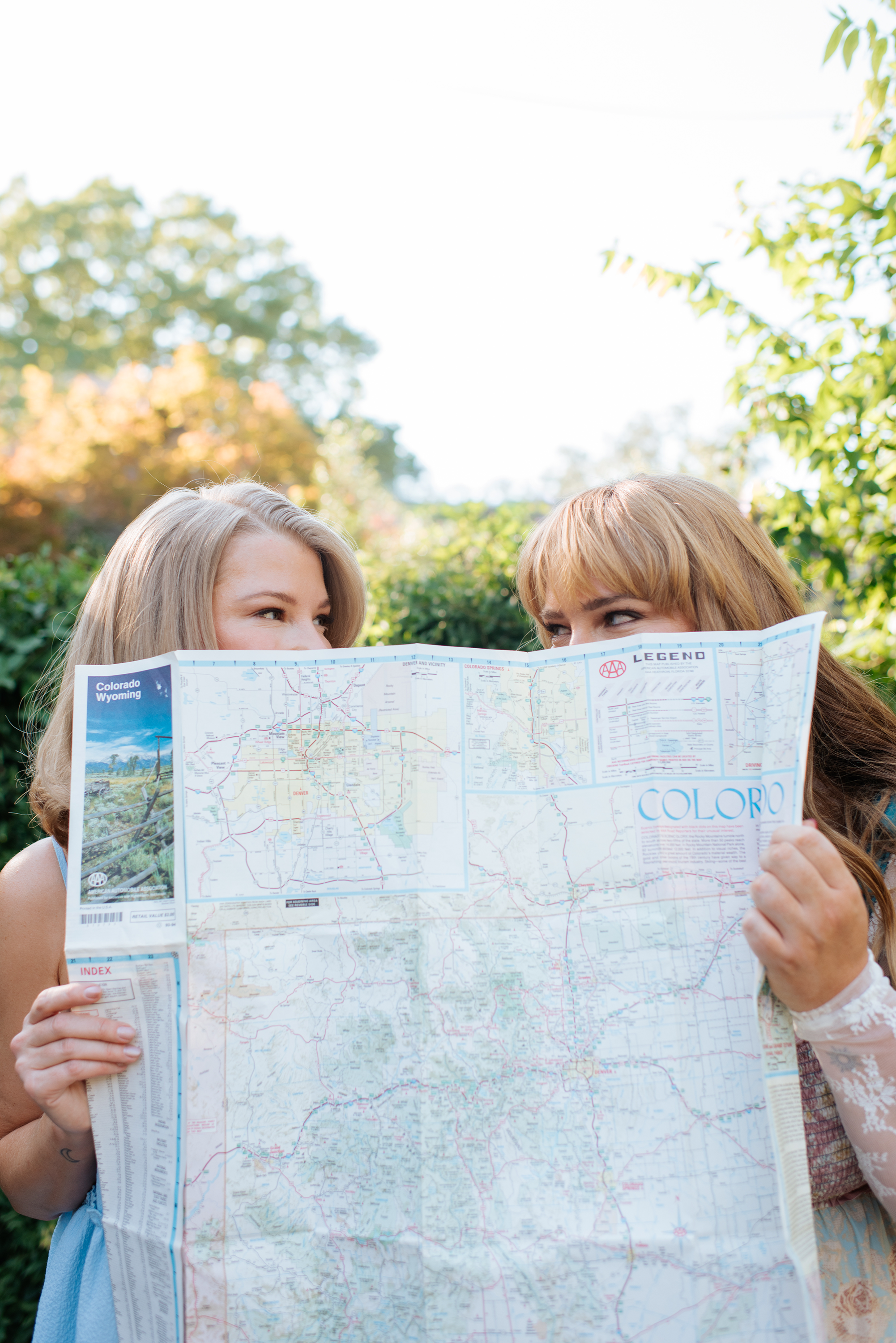 Two women smiling and holding a large map of Colorado in a park during daytime.