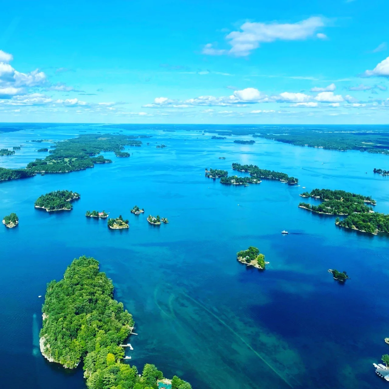An aerial view of a large lake with many small islands covered in green trees under a partly cloudy sky.
