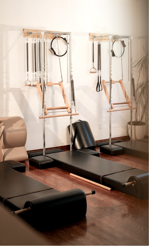 Pilates tower mats side by side in a wellness studio with a wooden floor and potted plant.