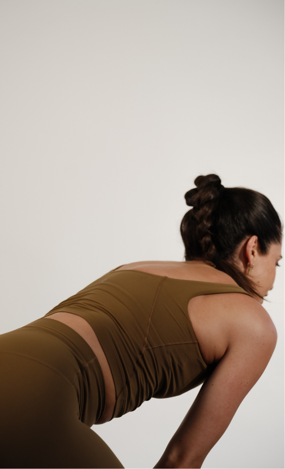 A woman in activewear bending forward in a stretching pose against a plain background.