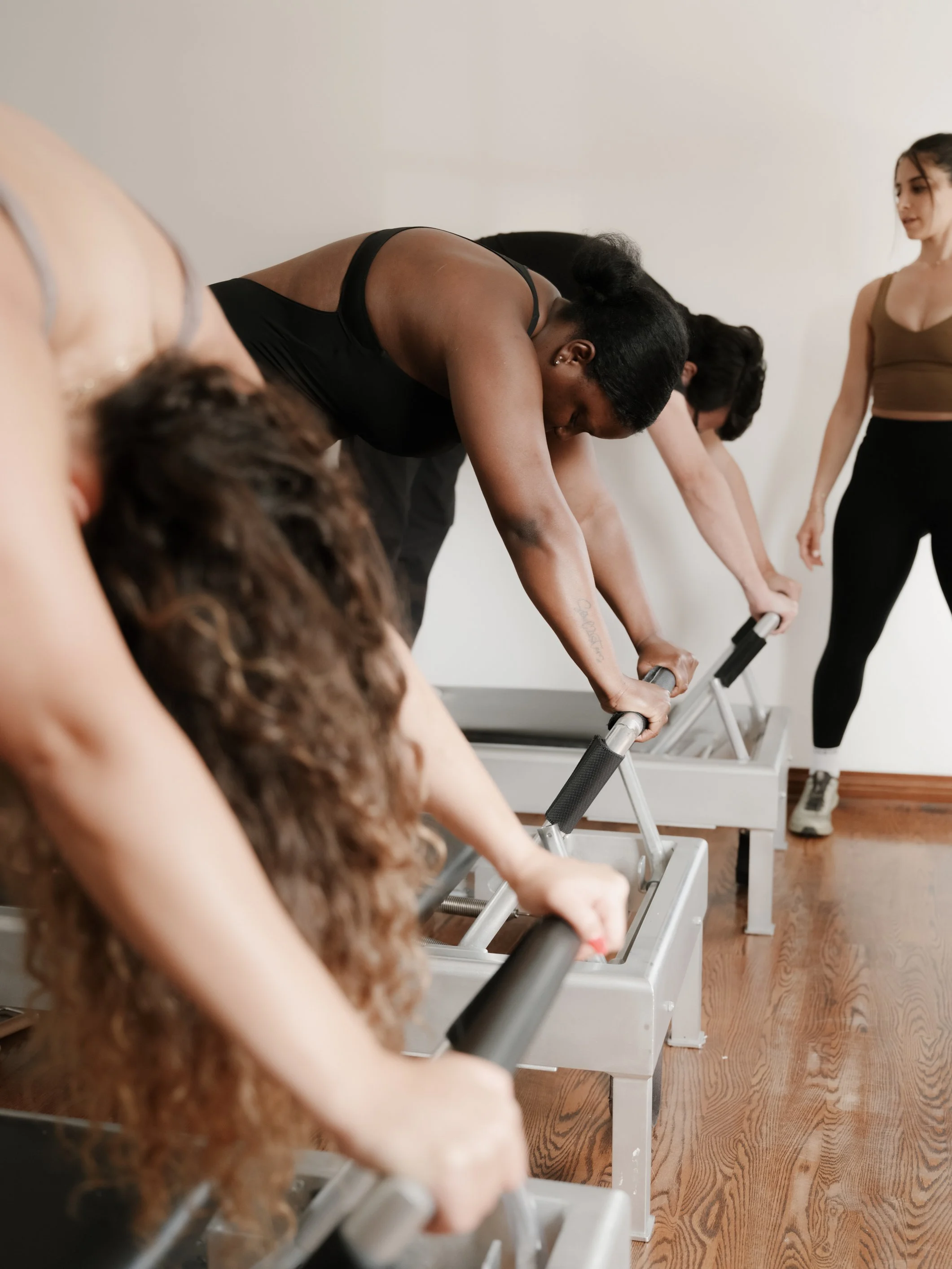 People exercising on pilates reformer machines in a class with an instructor.