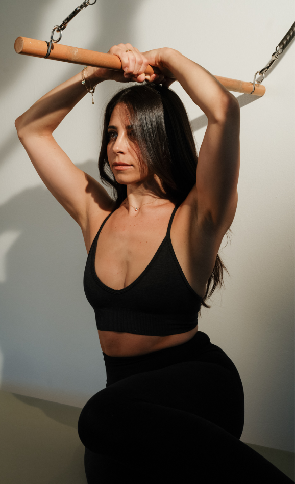 Woman in black sports bra and leggings stretching with a pull-up bar.