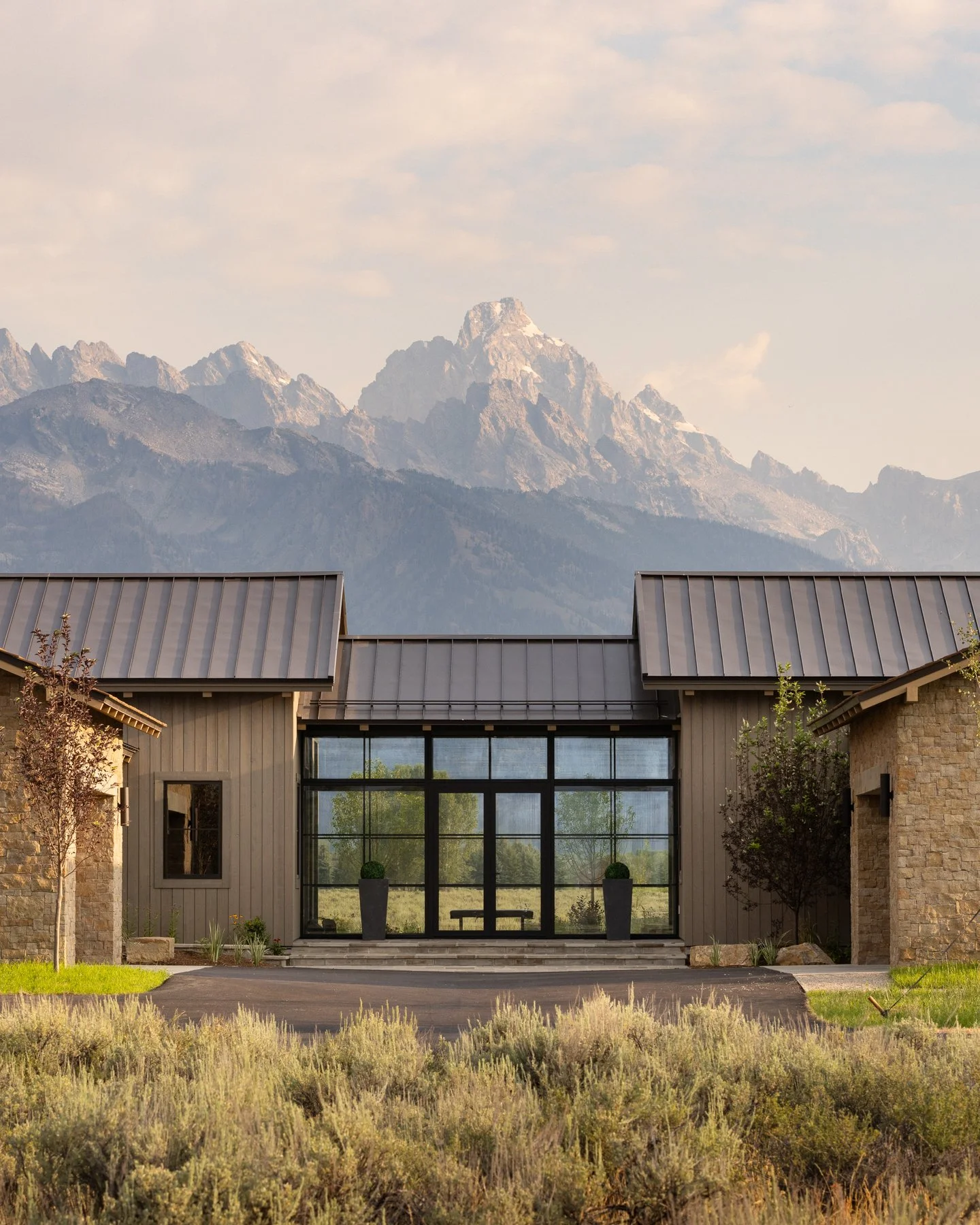 Modern house with large glass entrance, trees, and mountain range in the background.