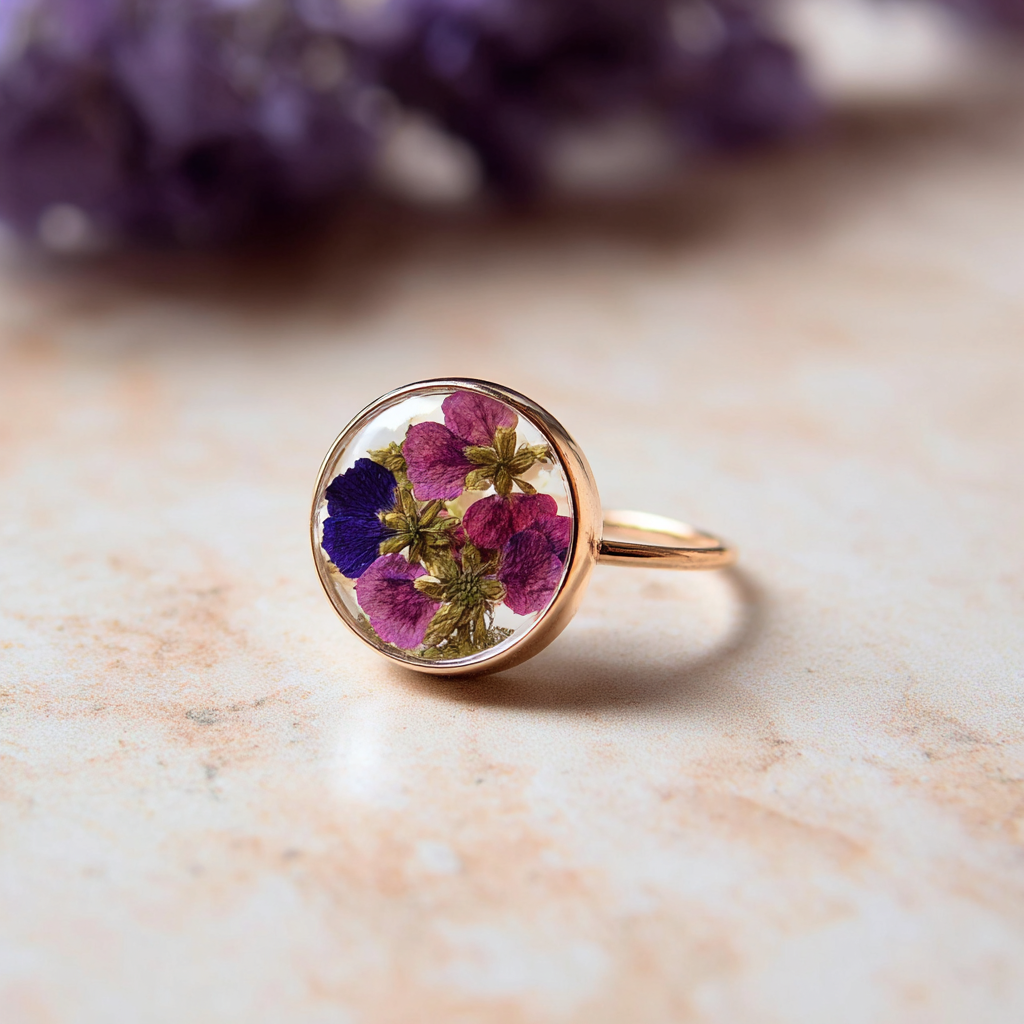 Flower jewelry. A gold ring with a clear round bezel containing pressed purple, pink, and blue flowers.