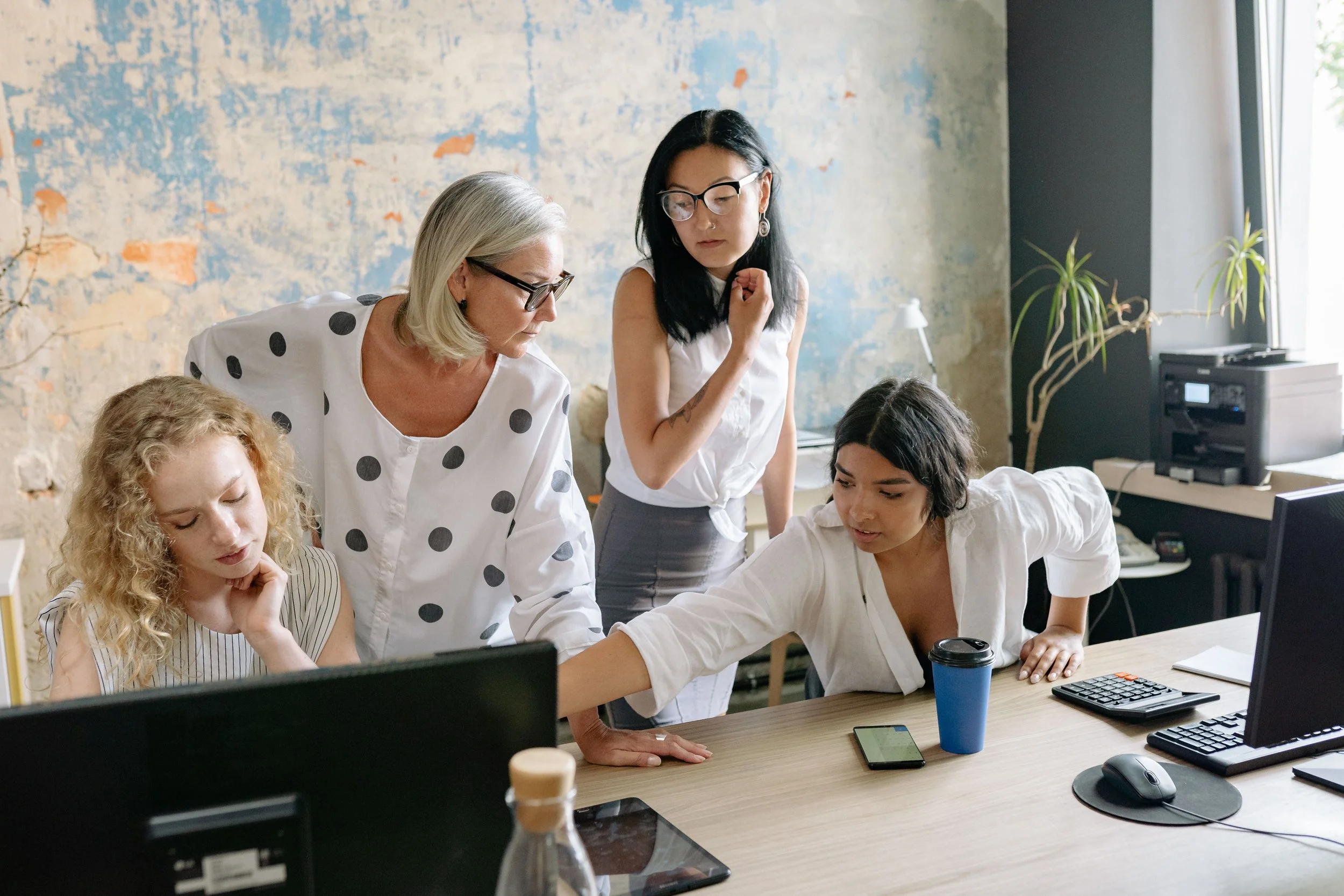 Group of women working together at a computer in an office.