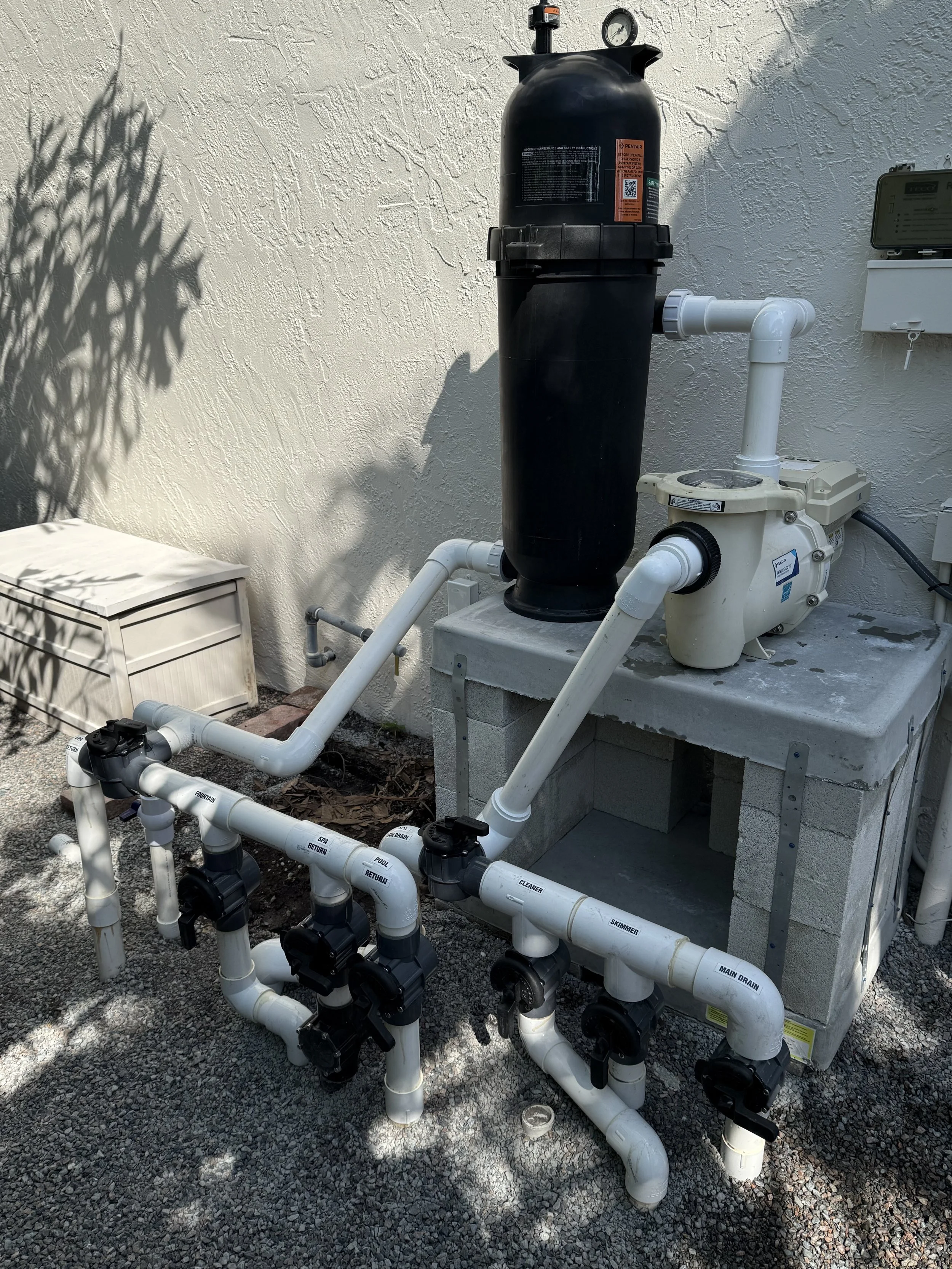 Swimming pool equipment with a filtration system and multiple PVC pipes for water circulation.