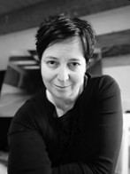 Black and white photo of a woman with short dark hair, smiling softly, wearing a black top, looking directly at the camera.