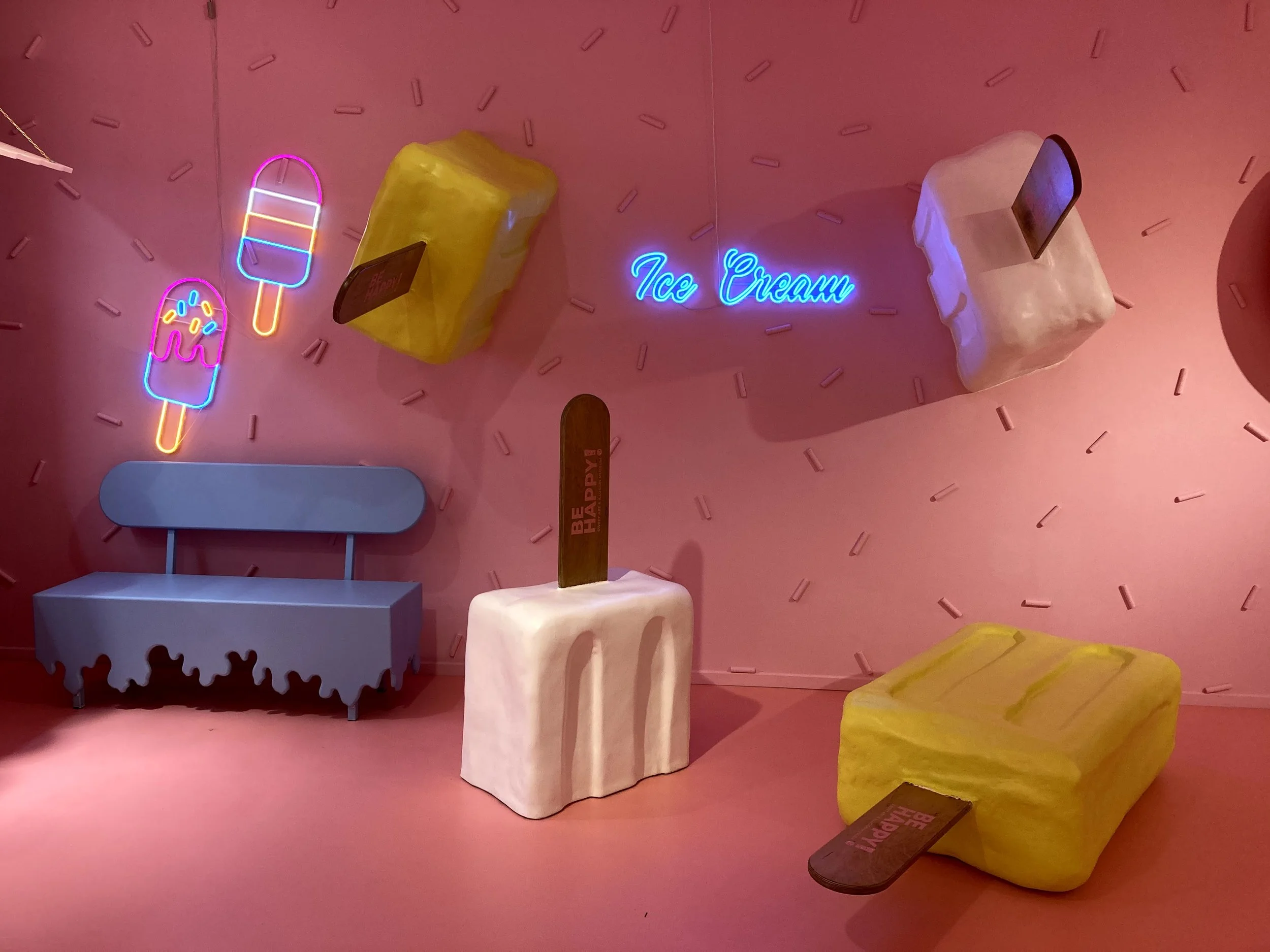 Colorful ice cream-themed decor with neon signs, ice cream bars, and large styrofoam ice cream blocks on a pink background.