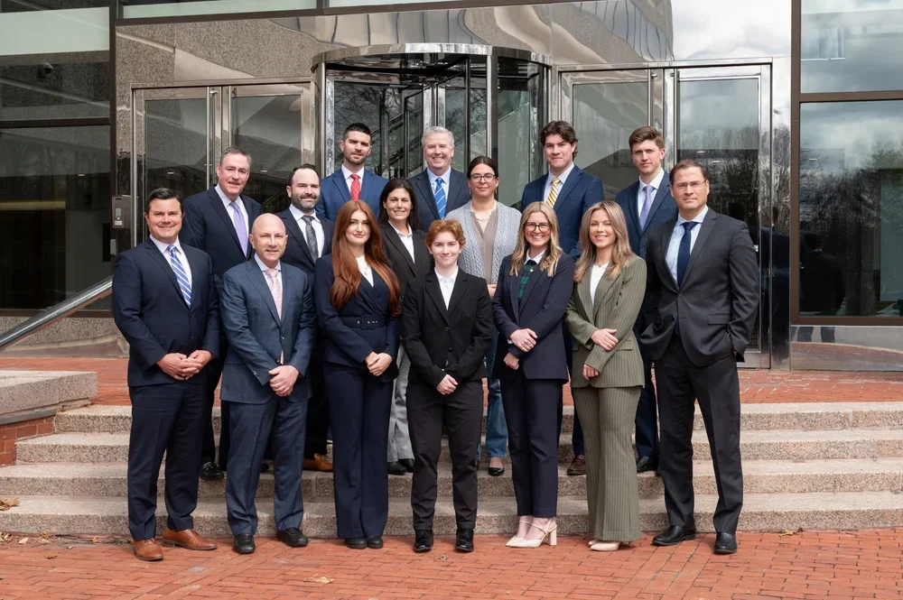 Group of fifteen professionally dressed people standing on steps in front of a modern office building.