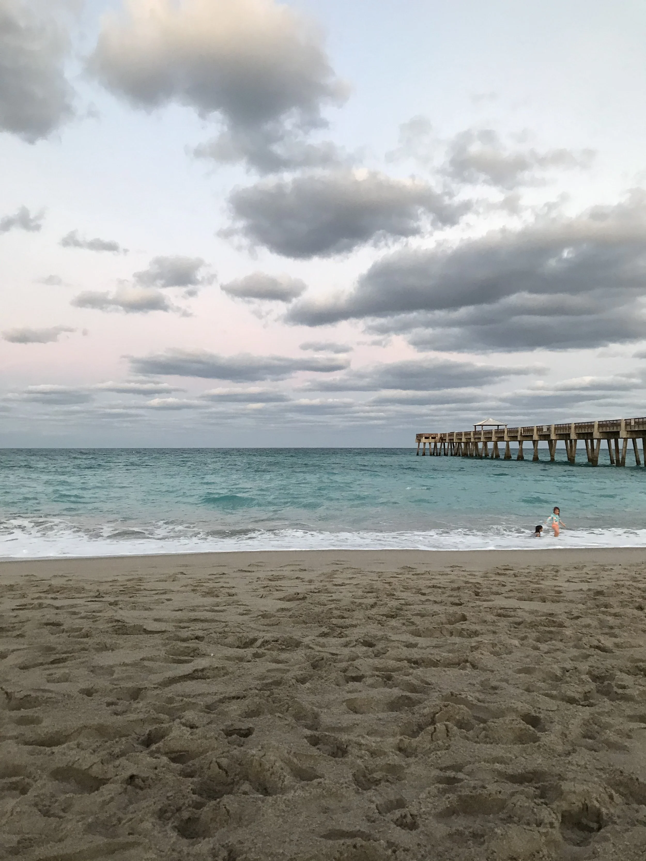 Photo of Juno Beach pier and the ocean, two small children are playing in the shore break.