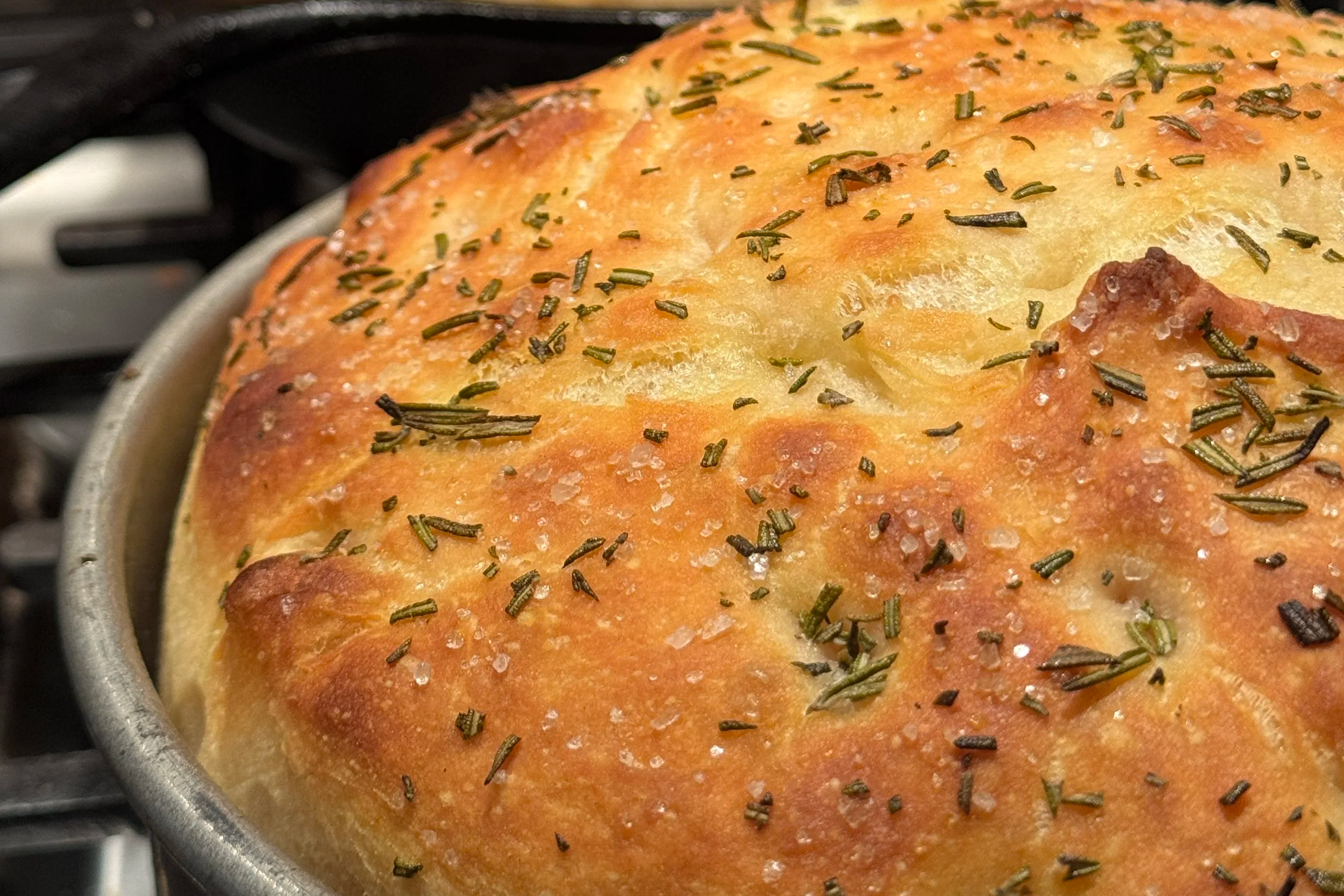 Two freshly baked rosemary and sea salt focaccia bread loaves in baking dishes cooling after baking.