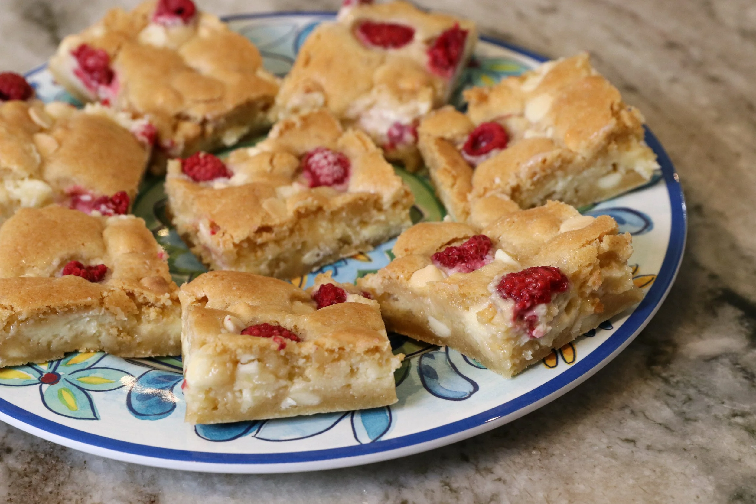 A colorful plate with sliced raspberry white chocolate blondies on a marble countertop.
