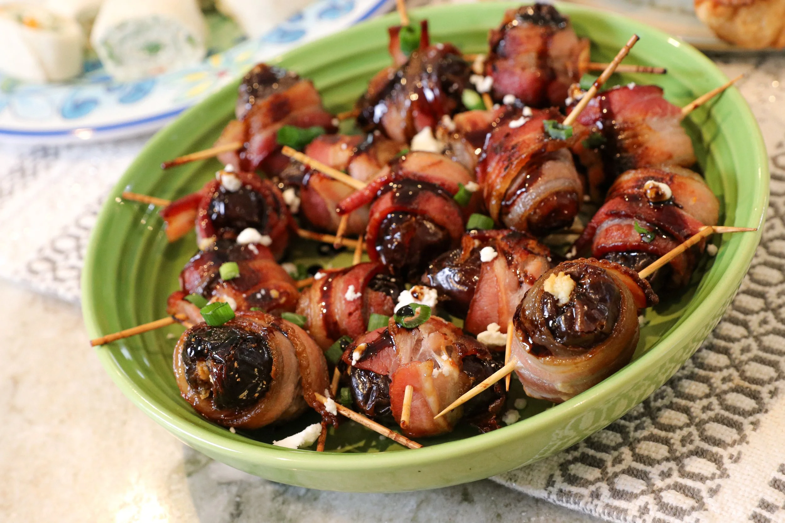 Bacon-wrapped stuffed date appetizers garnished with chopped green onions on a green oval dish.