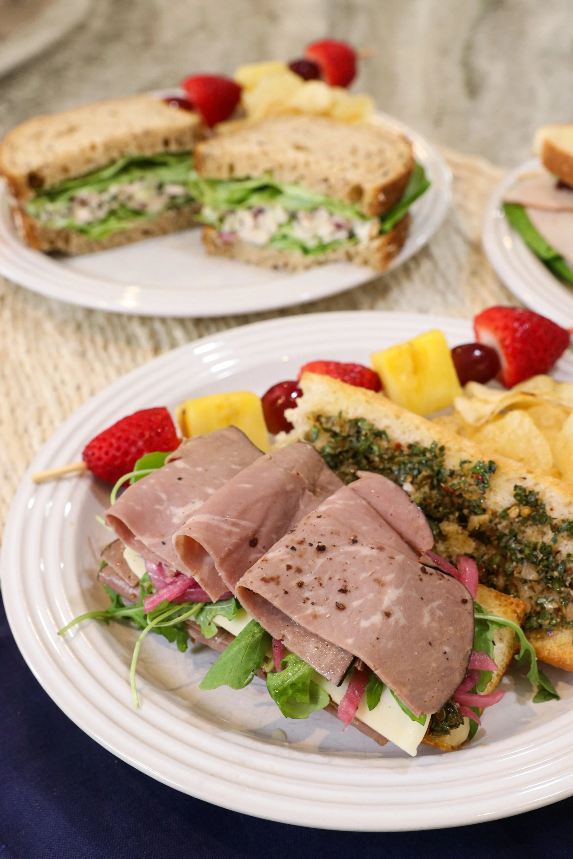 Plates with sandwiches, fresh strawberries, pineapple, grapes, and chips.