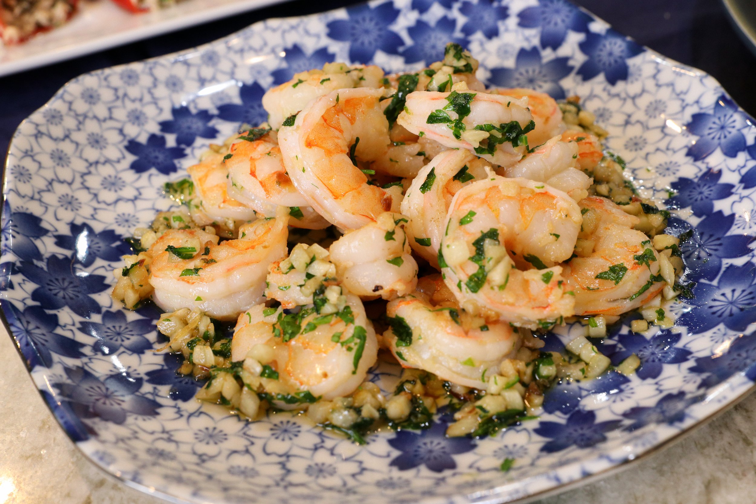 Shrimp dish garnished with chopped herbs on a decorative blue and white plate.