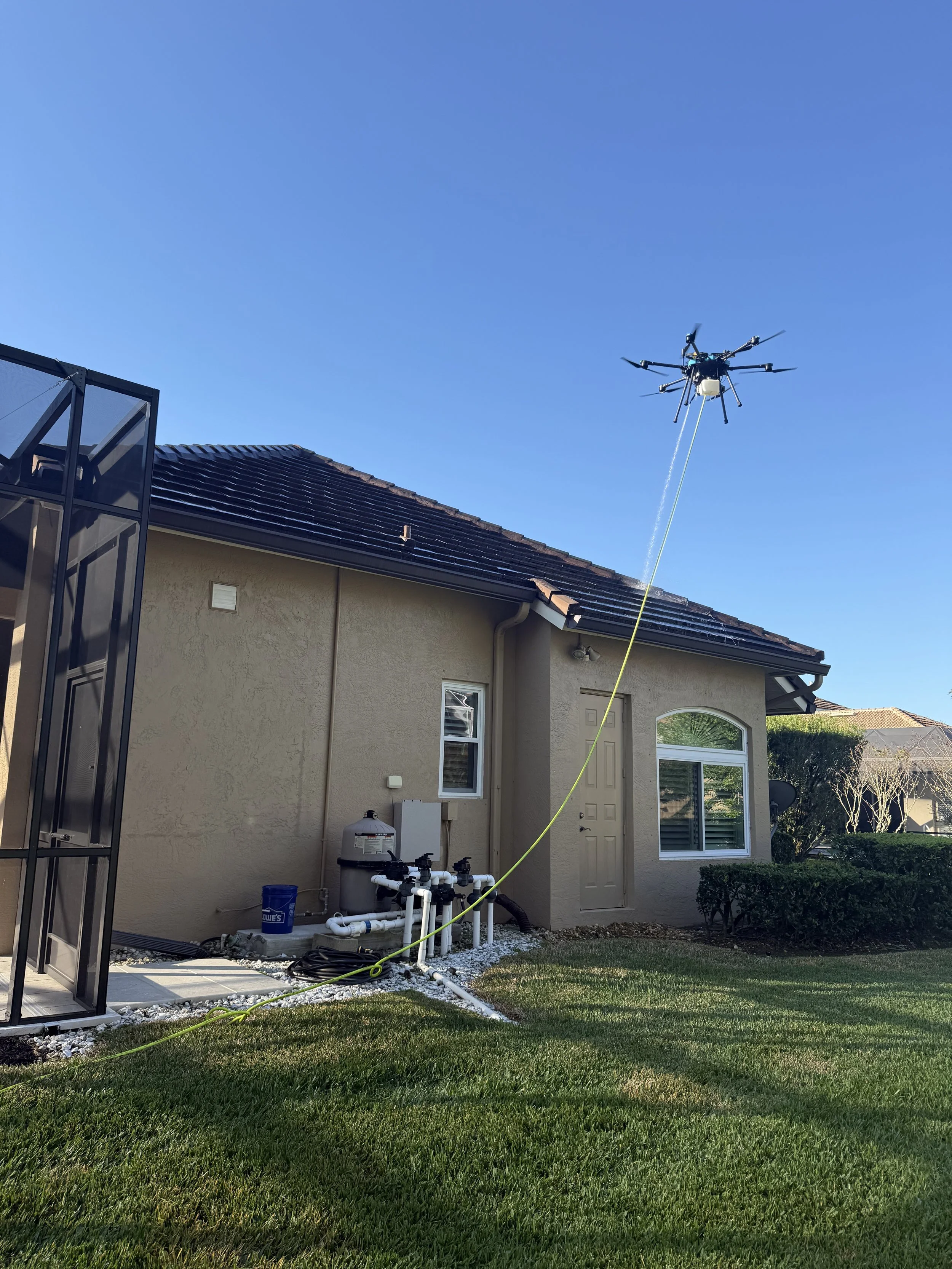A drone is spraying cleaning solution onto the exterior of a residential building