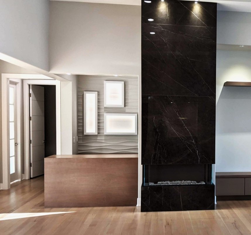 Modern living room with a dark marble fireplace, light wood flooring, and decorative wall art with three illuminated frames.