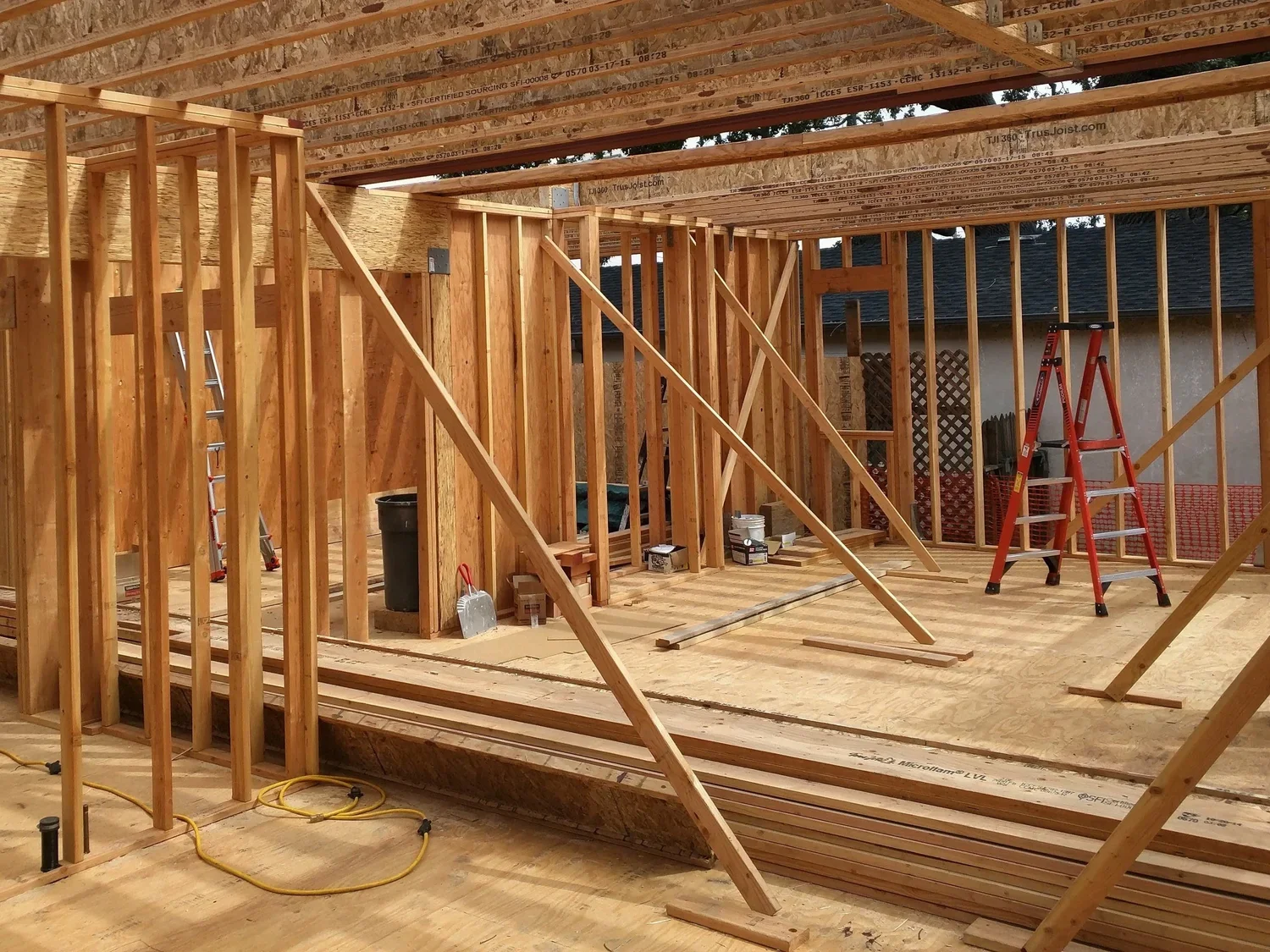 Interior view of a house under construction with wooden framing, a ladder, and construction tools.