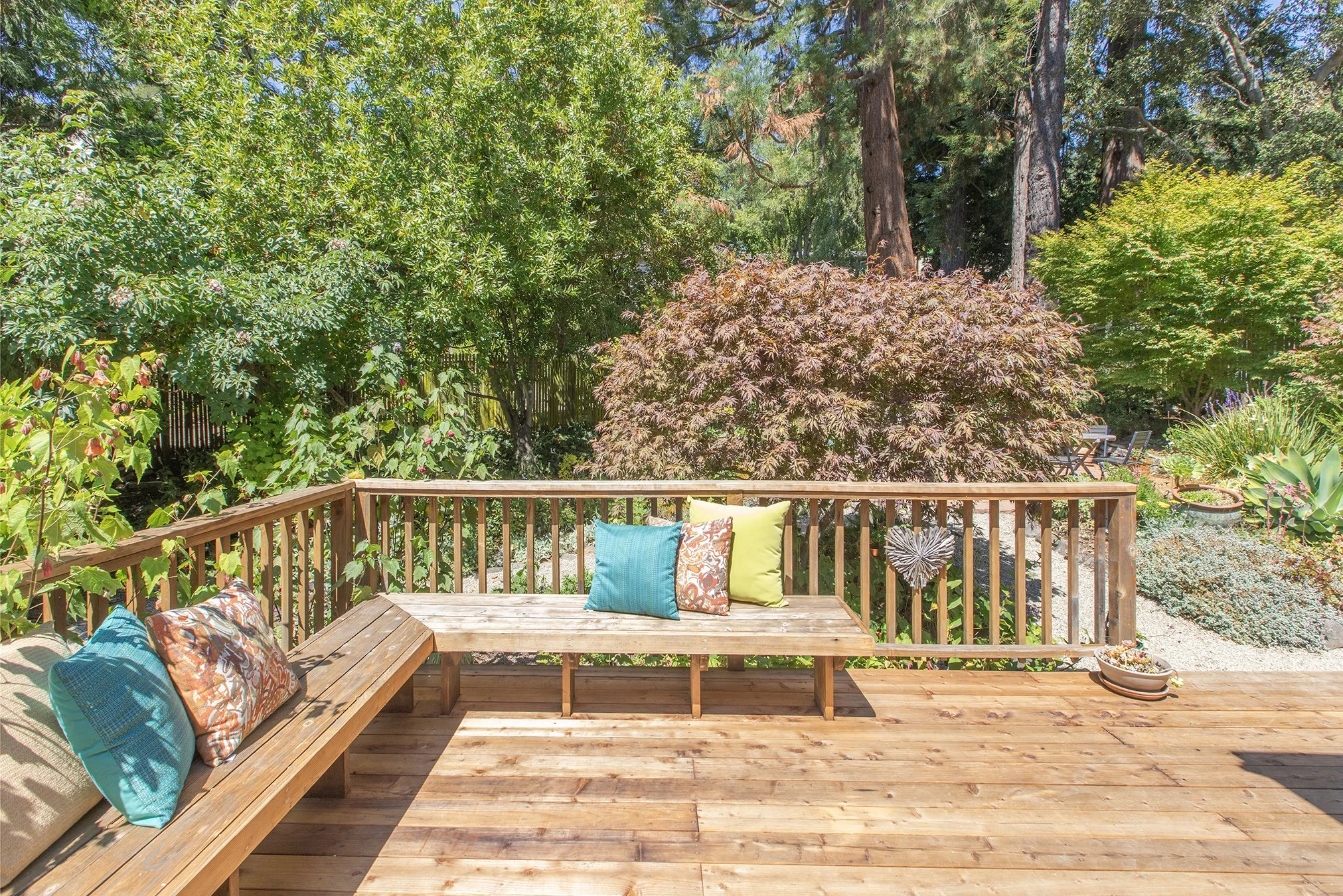 Wooden deck with colorful cushions and a garden with trees and plants in the background.