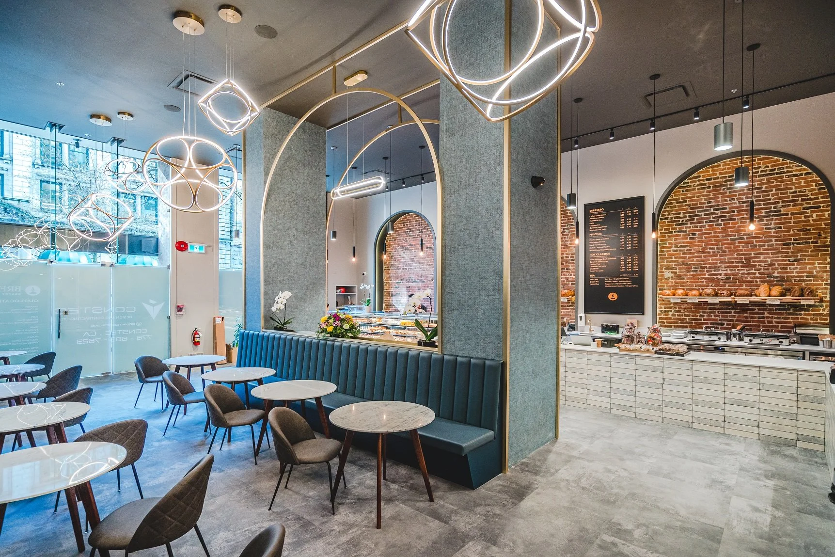 Modern coffee shop interior with tables, chairs, decorative lighting, brick accent wall, and a menu board.