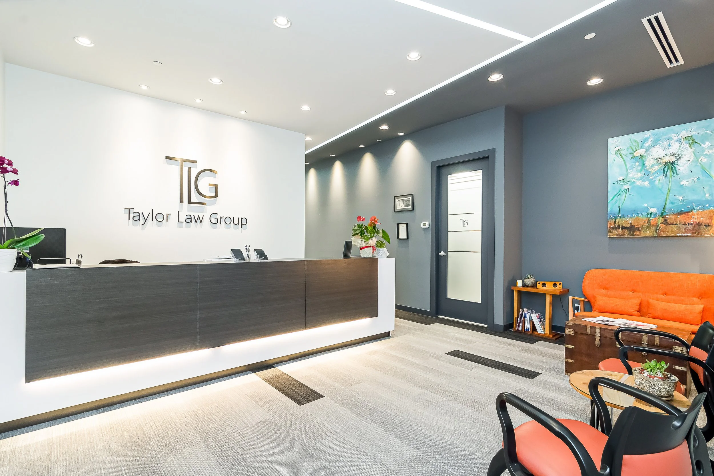 Reception area of Taylor Law Group with a modern desk, gray and white walls, a seating area with orange and black chairs, and artwork on the wall.