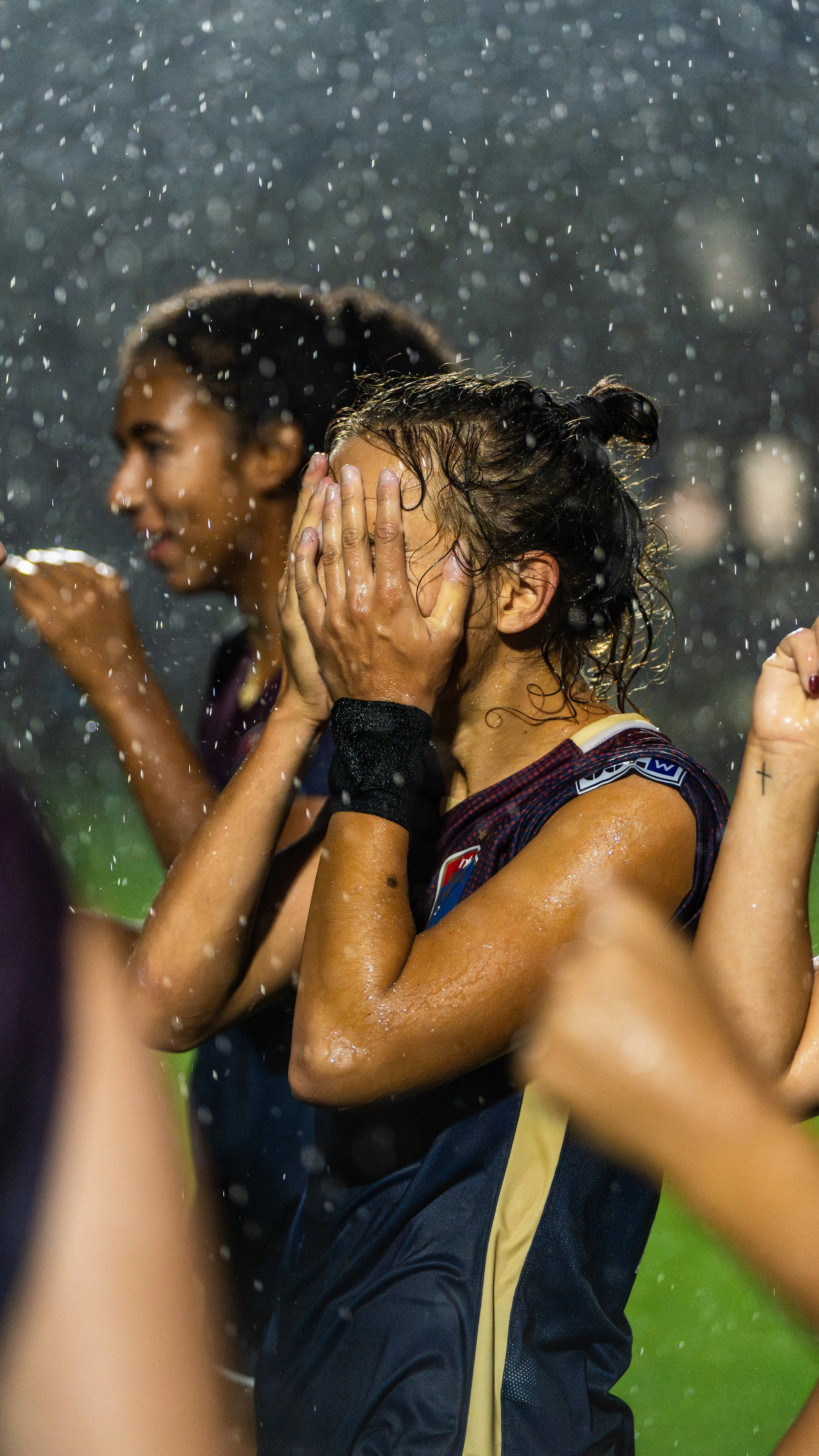 Female athlete hugging herself after a game in the rain, surrounded by other players.