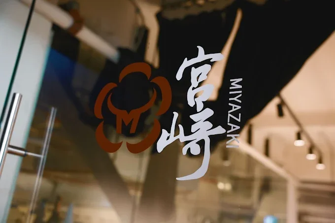 Close-up of a glass with a logo and Japanese characters, reading 'MIYAZAKI' and '宮崎', in the restaurant entrance door.