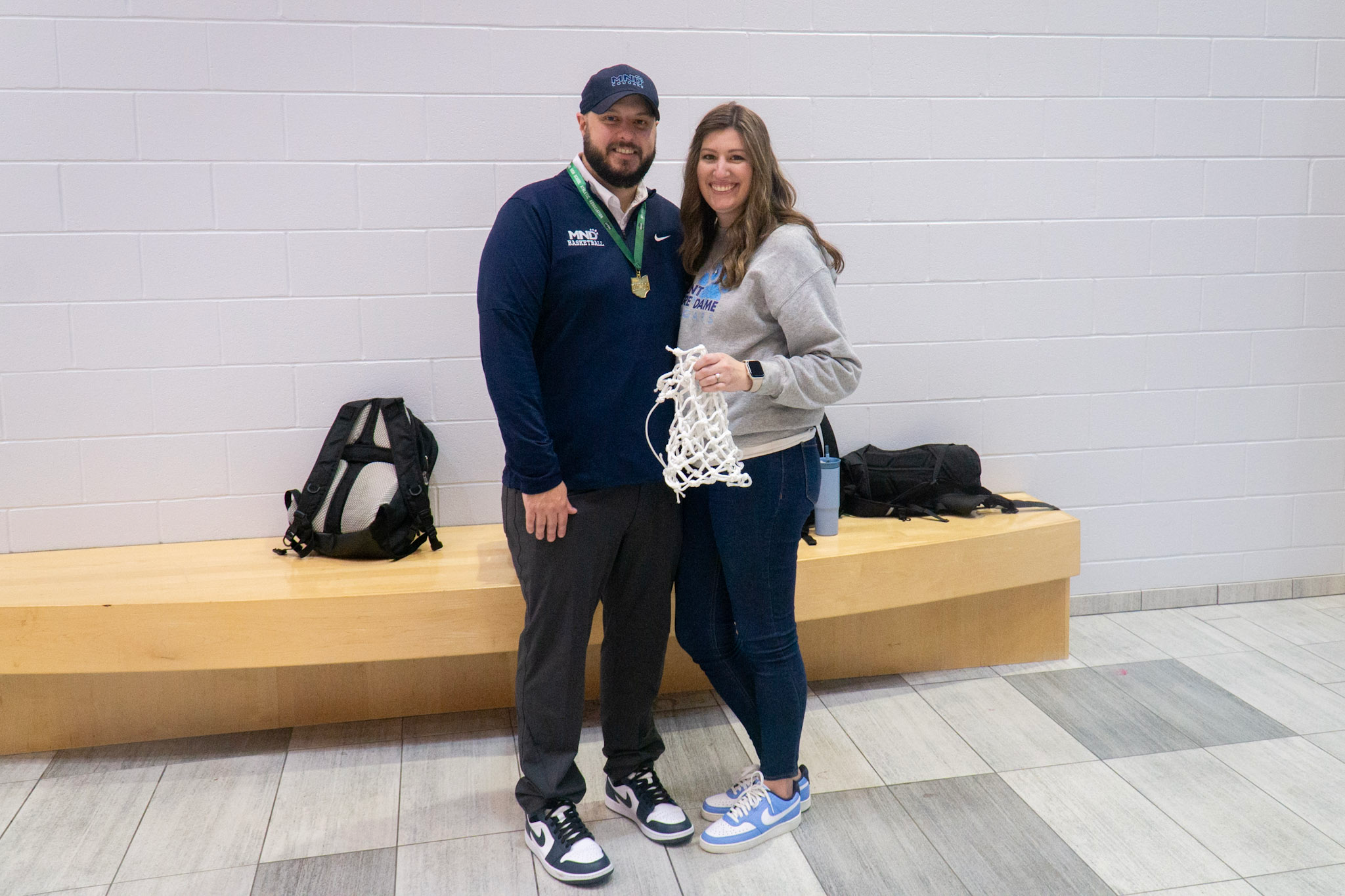 Woman and her husband, a basketball coach, after a victory holding the cut-down net and wearing a medal.