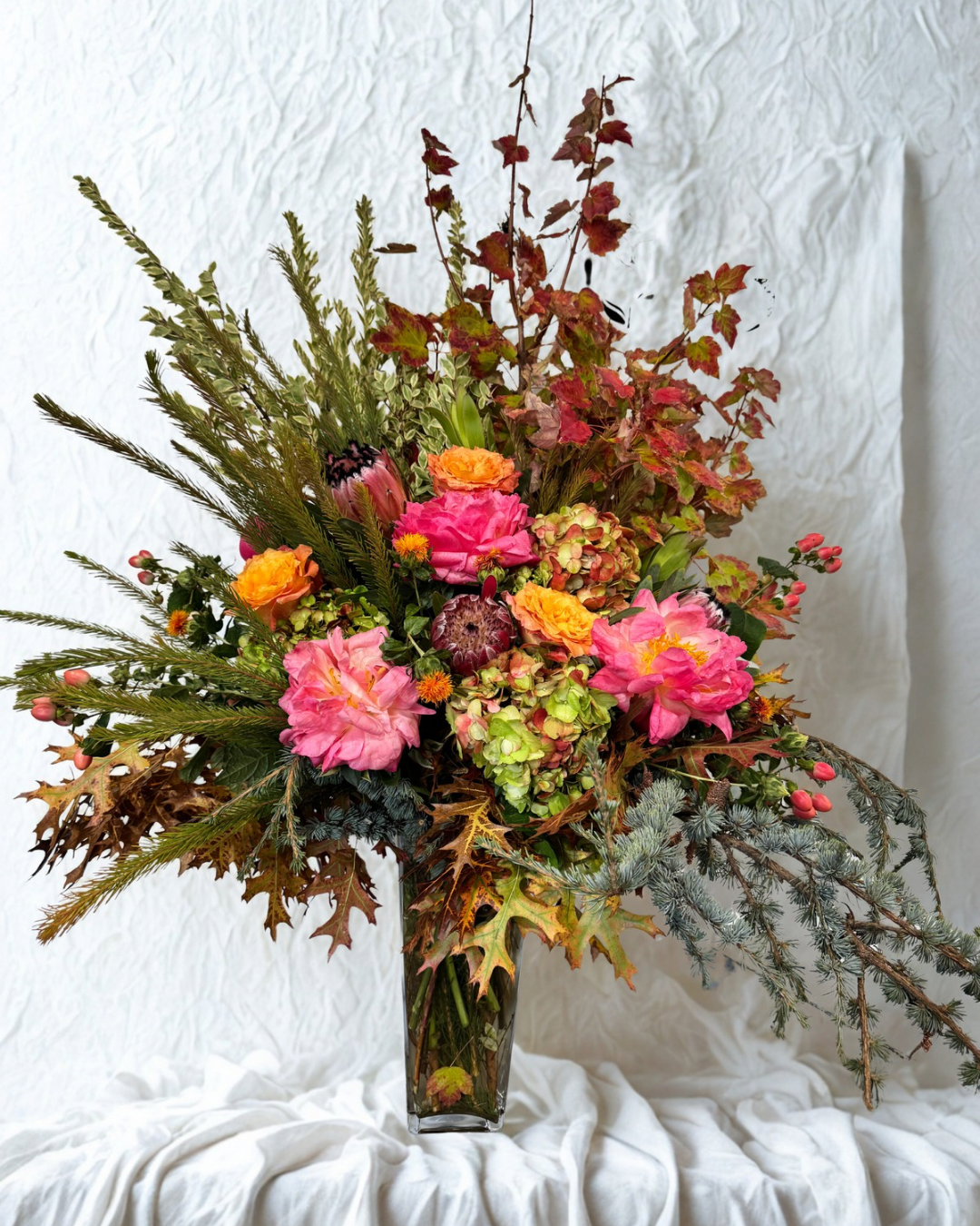 A bouquet of pink roses, white hydrangeas, and assorted greenery in a glass vase placed on a wooden table in front of a brick fireplace.