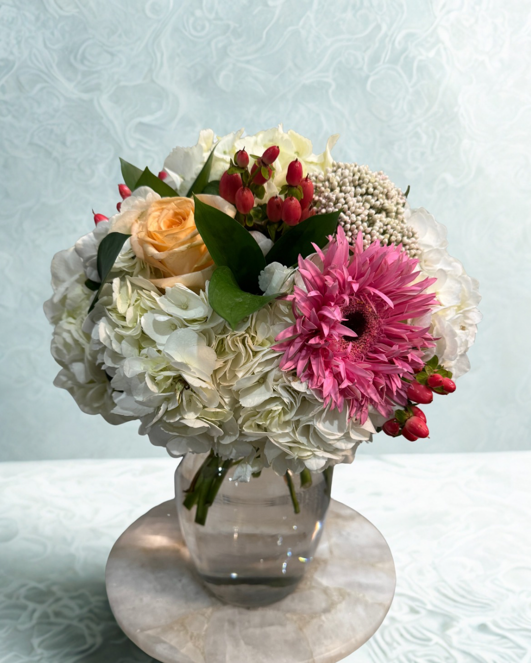 Bouquet of white flowers with green leaves rests on a light green vintage drawer against a plain wall.