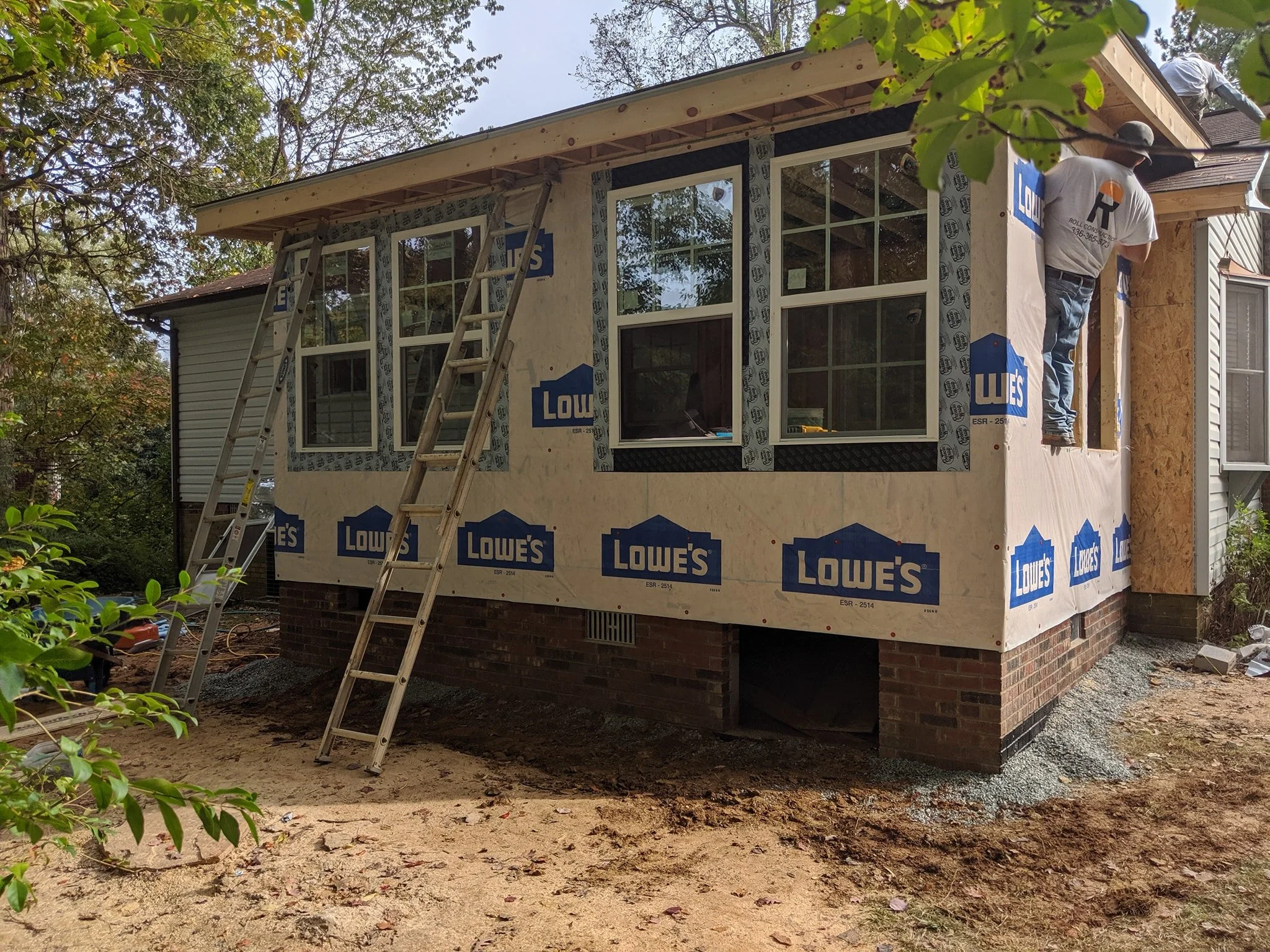 man working on home addition in grey t-shirt and jeans with two metal ladders leaning against the house