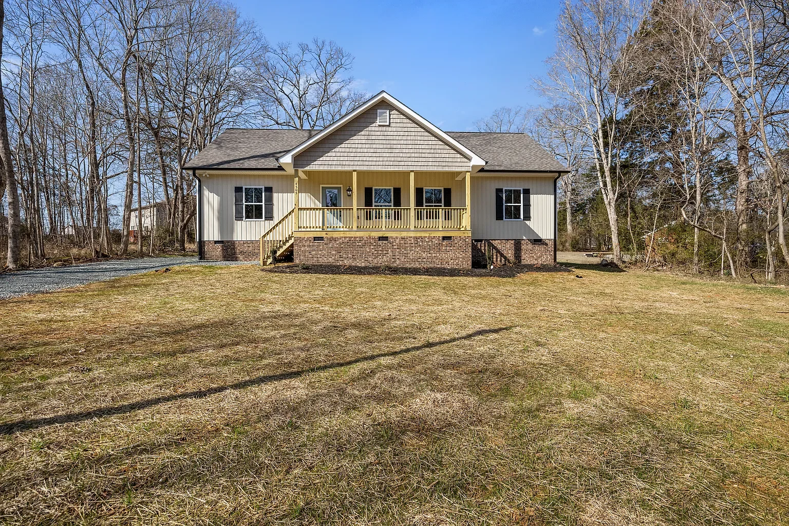 A new constructed house with brick foundation and front porch in between tall trees. Front yard with gravel gravel to the side